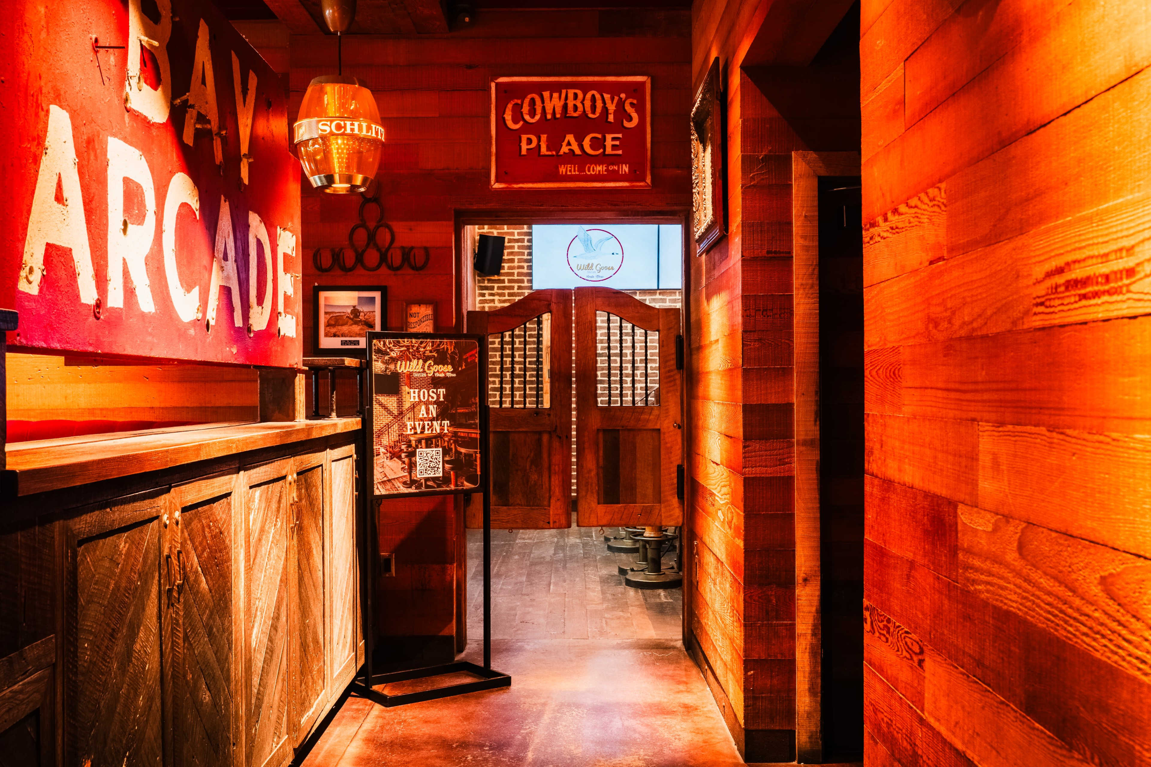 The image shows a rustic hallway leading to a wooden double door, with signs and decorations related to an arcade and a venue called "Cowboy's Place."