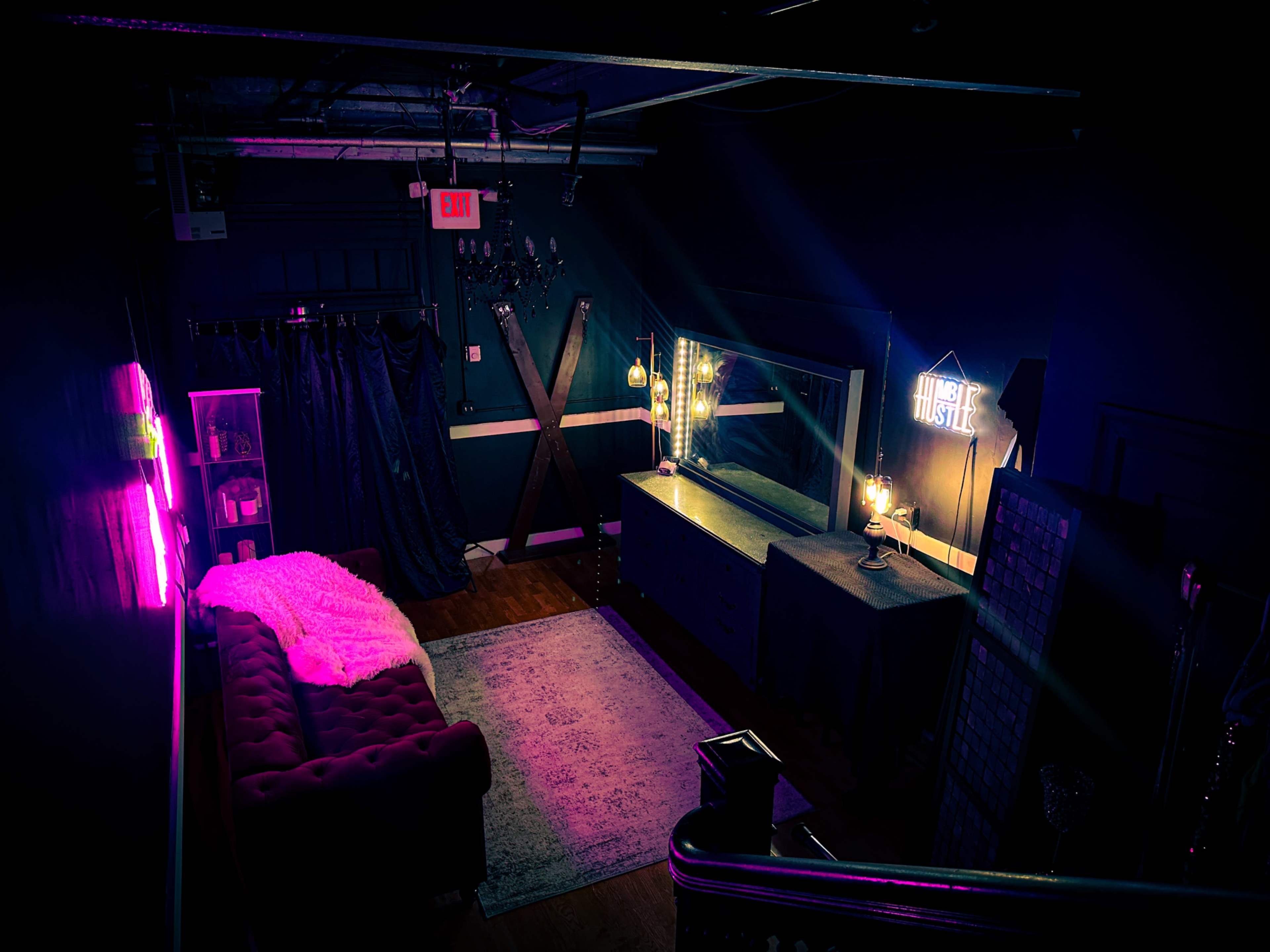 A dimly lit room with a pink sofa, a dresser with a mirror, and neon signs on the walls.