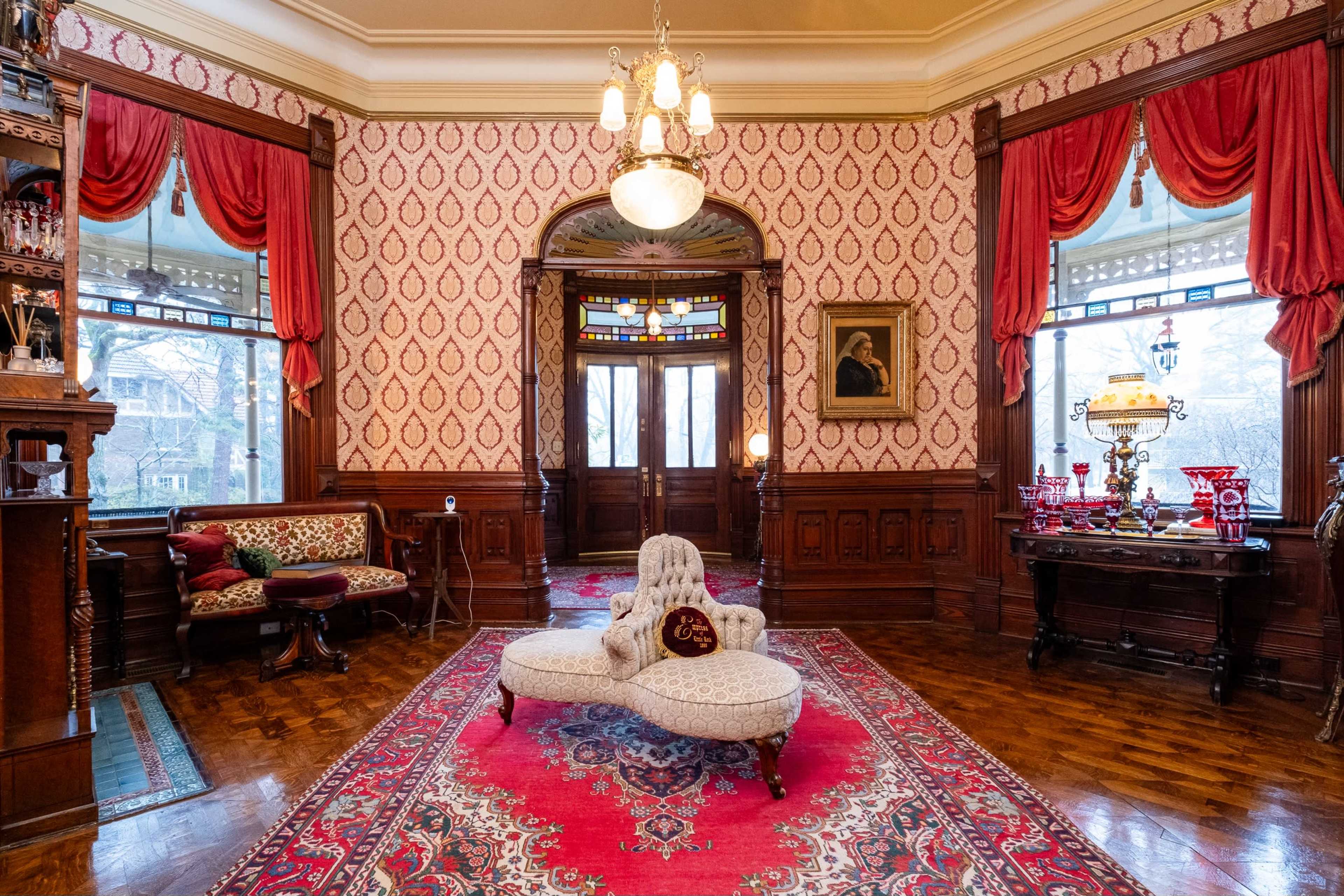 The image shows an ornate parlor with patterned wallpaper, a decorative chandelier, a vintage chaise lounge, and elaborate furnishings.