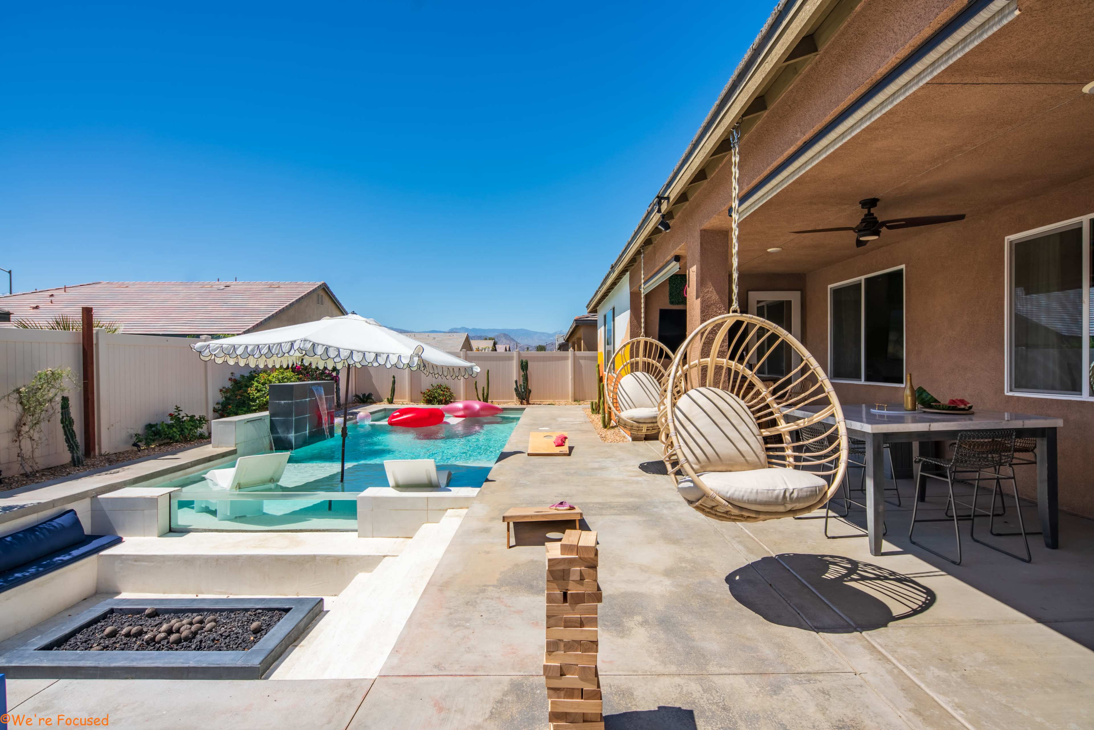A backyard with a swimming pool, hanging chairs, and a shaded area with a table and chairs.