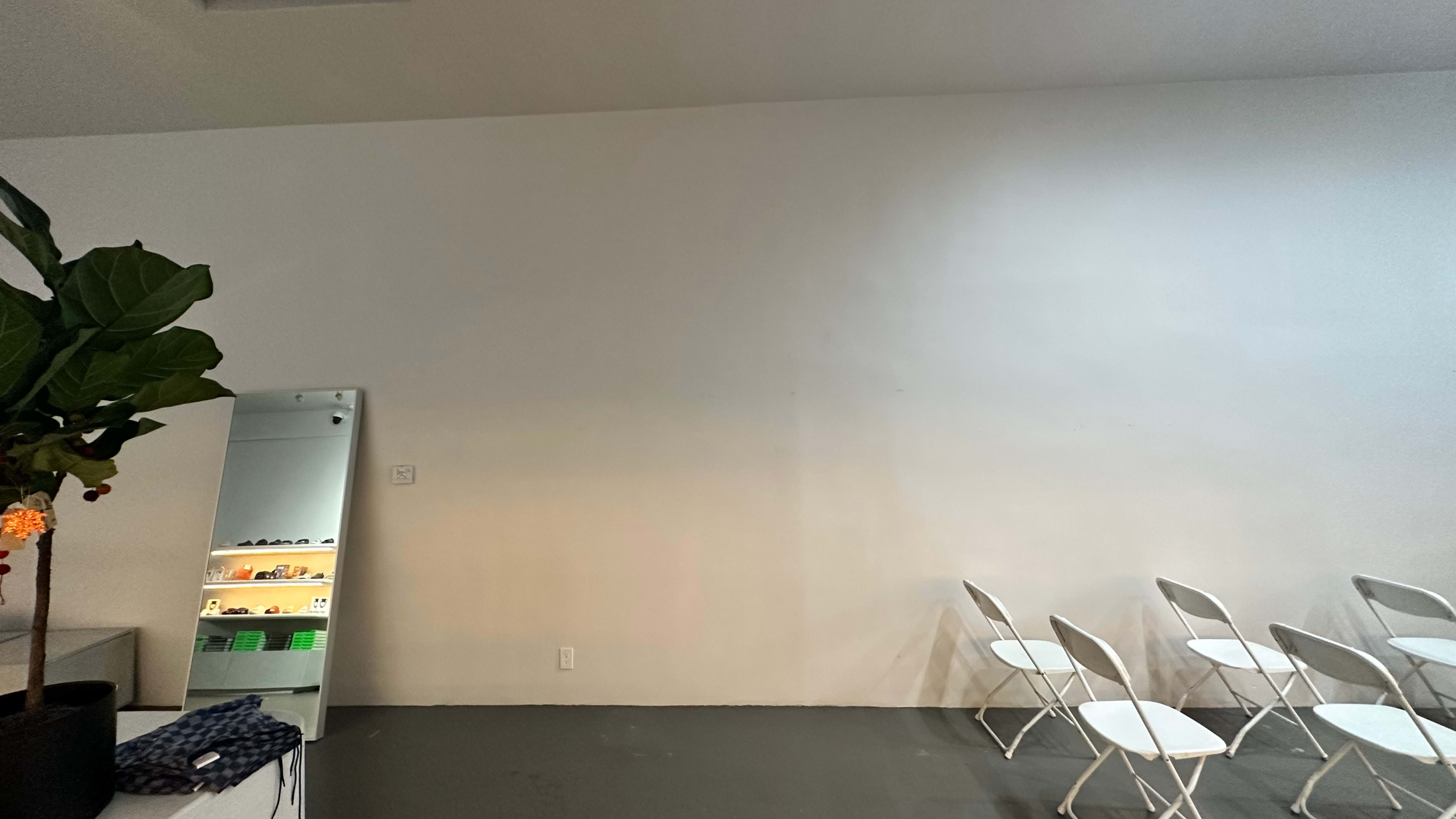 The image shows a plain white wall with a mirror and several folding chairs positioned nearby.