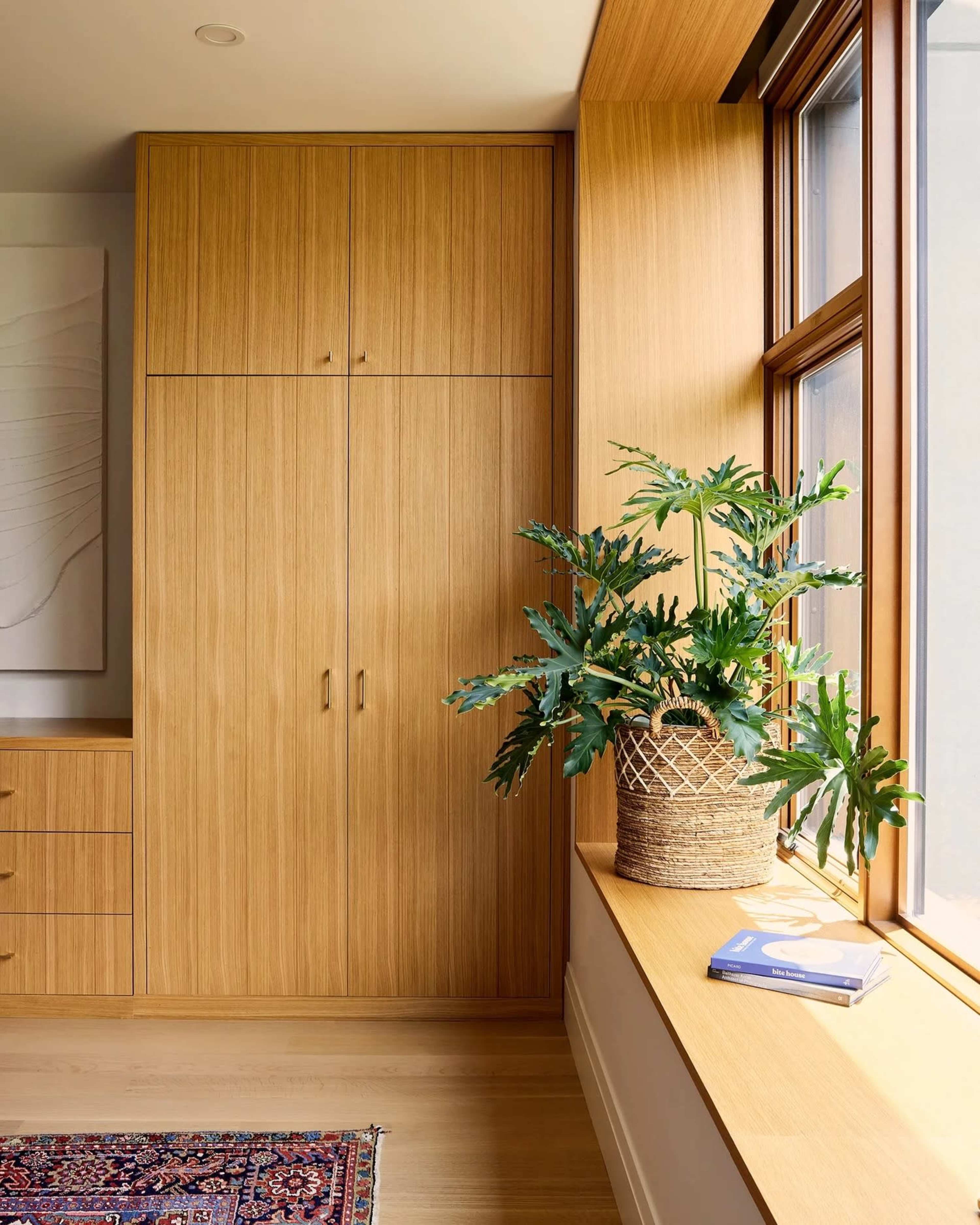 The image shows a modern interior with wooden cabinetry, a large window, and a potted plant on a window sill.