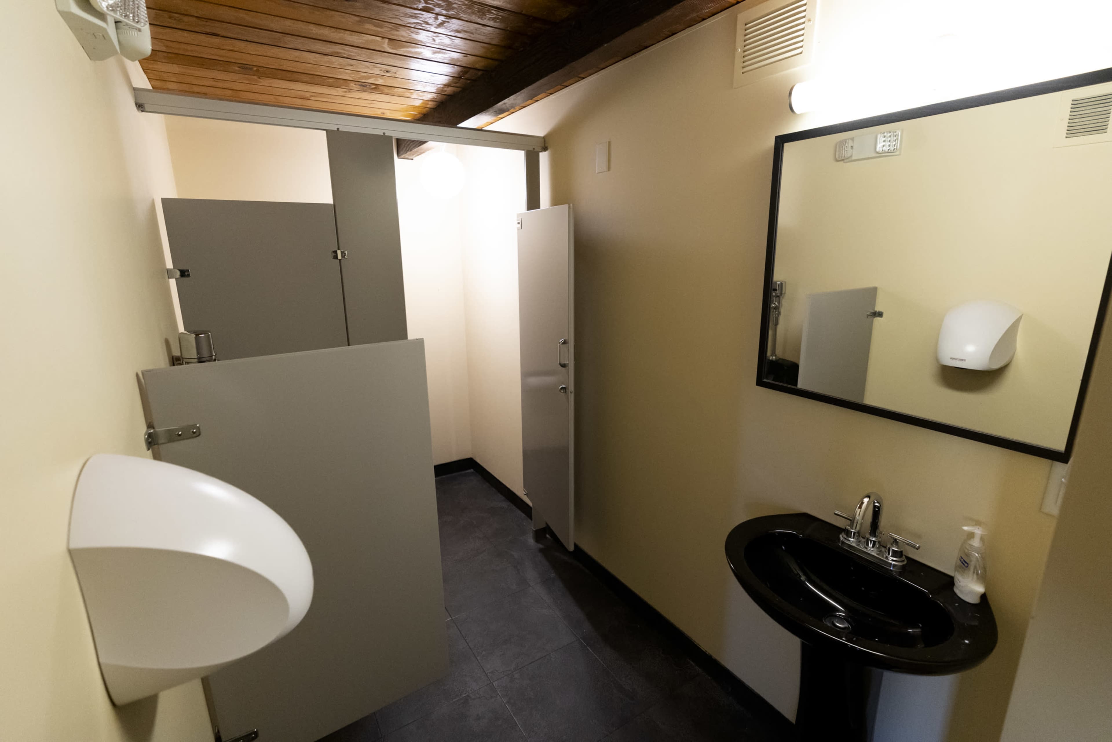 A minimalist bathroom with a sink and two stalls enclosed by gray partitions.