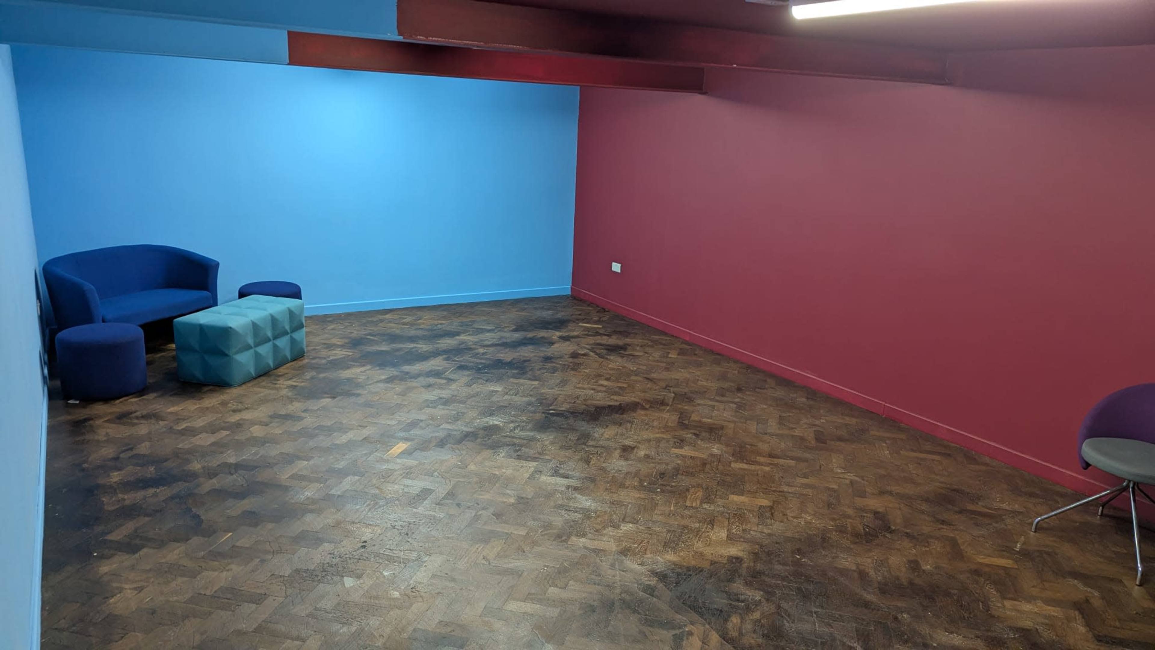 The room features a blue wall and a maroon wall, with a seating area consisting of two blue chairs, a blue ottoman, and a light blue cube table on a wooden floor.