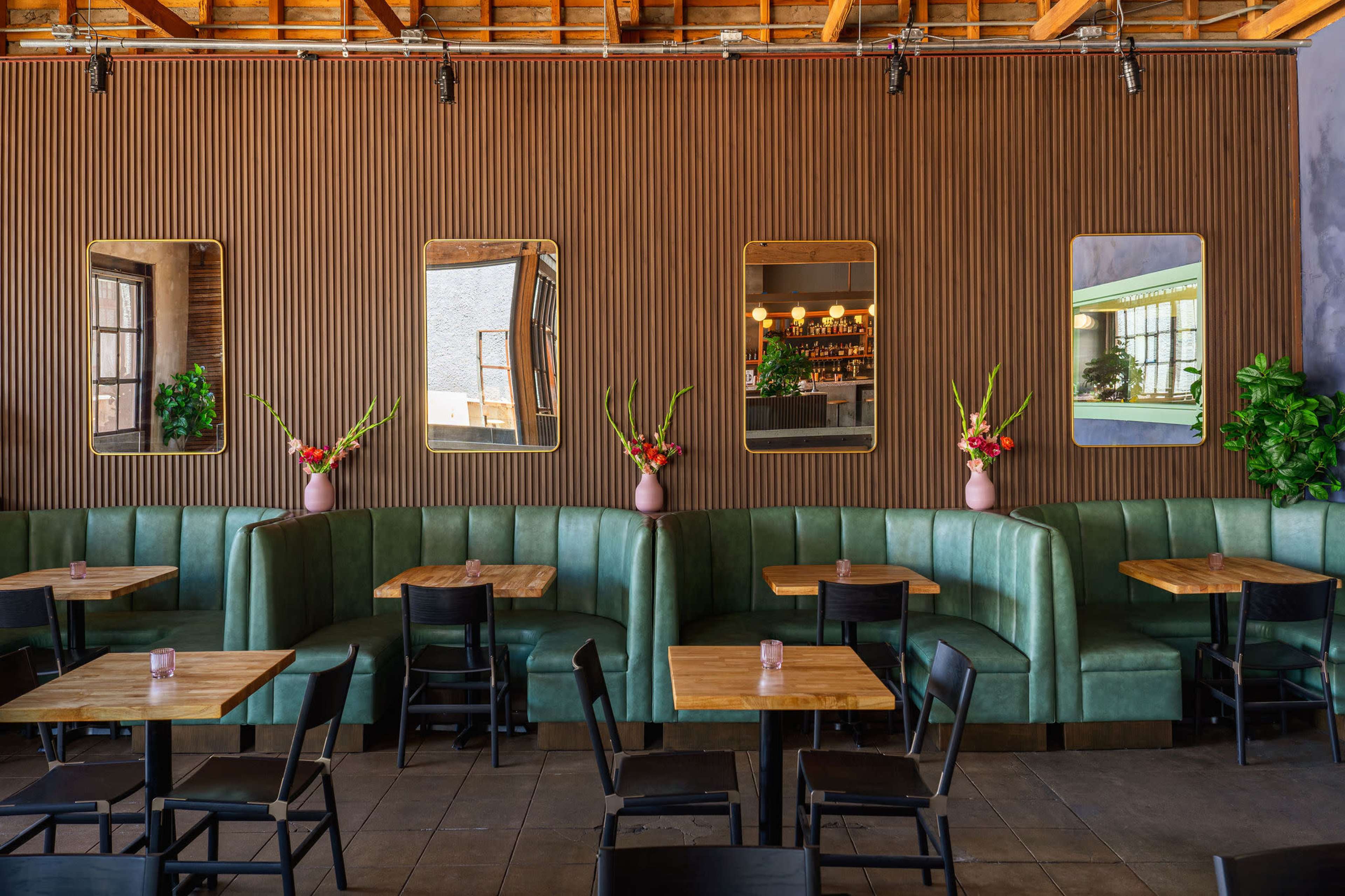 A restaurant interior featuring green seating booths, wooden tables, and large mirrors set in a textured wooden wall.