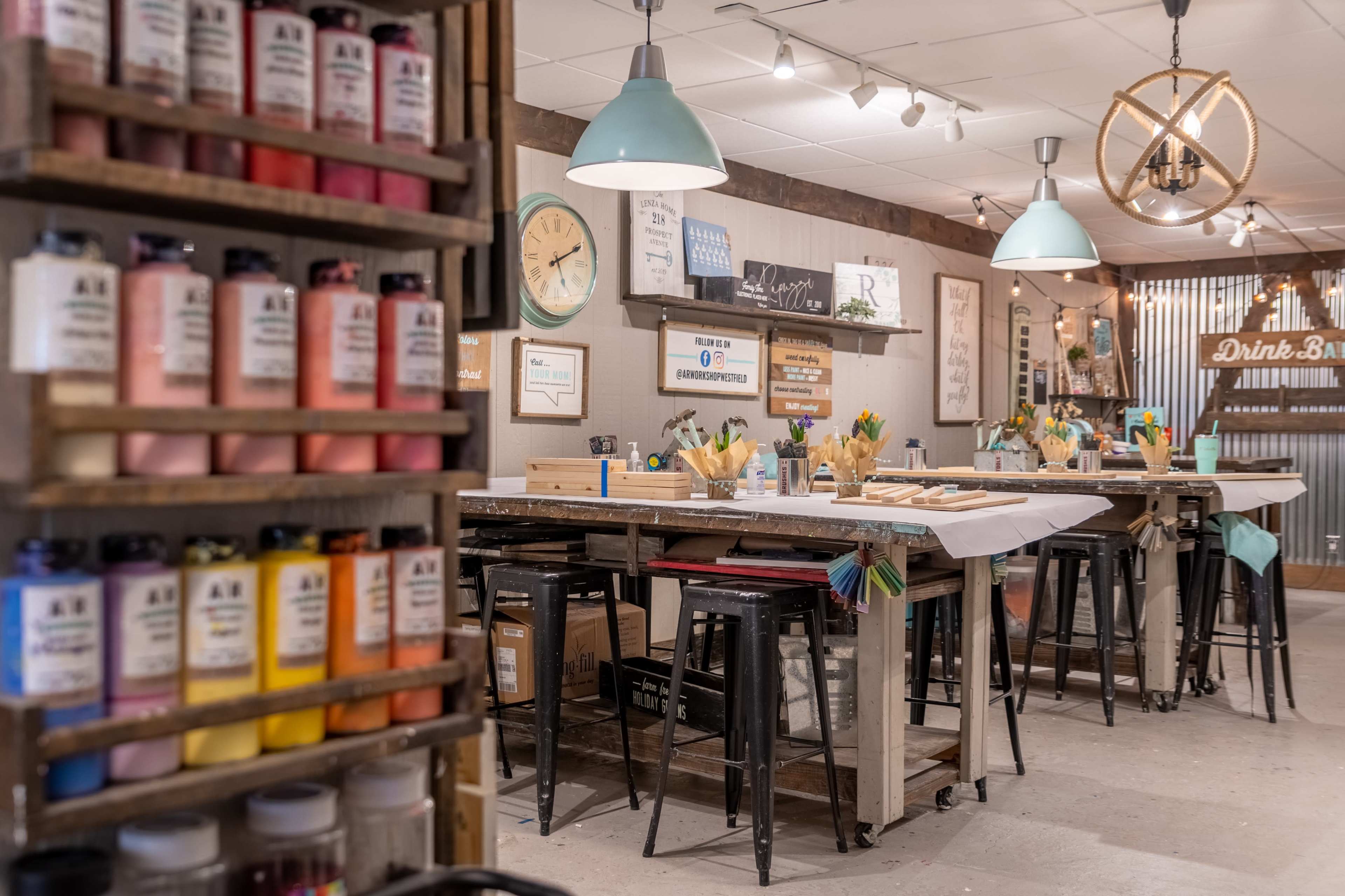 The image shows a colorful craft studio equipped with multiple work tables, paint supplies, and various crafting tools neatly organized.