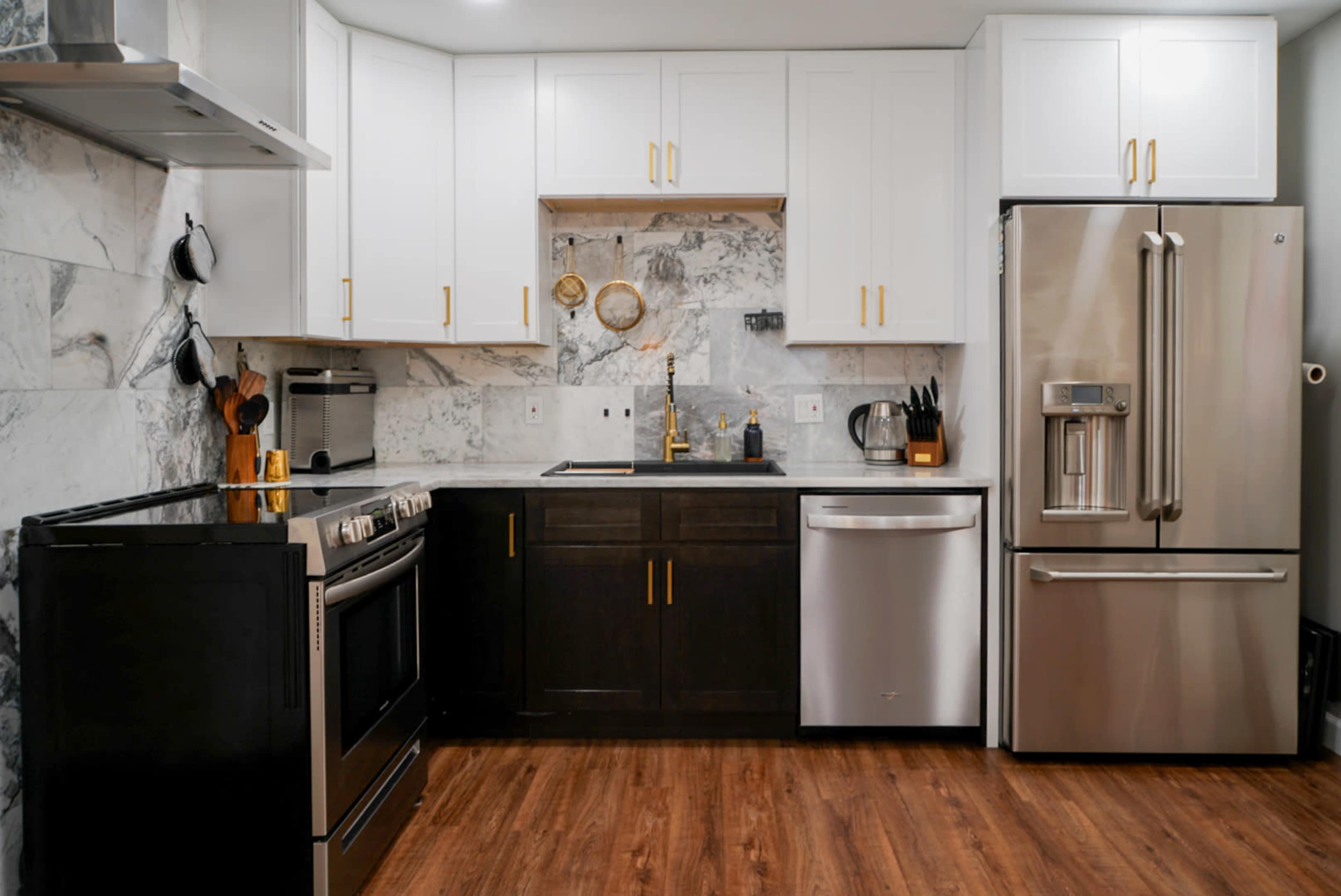 The image shows a modern kitchen featuring a combination of dark and light cabinetry, a stainless steel fridge, and a marble backsplash.