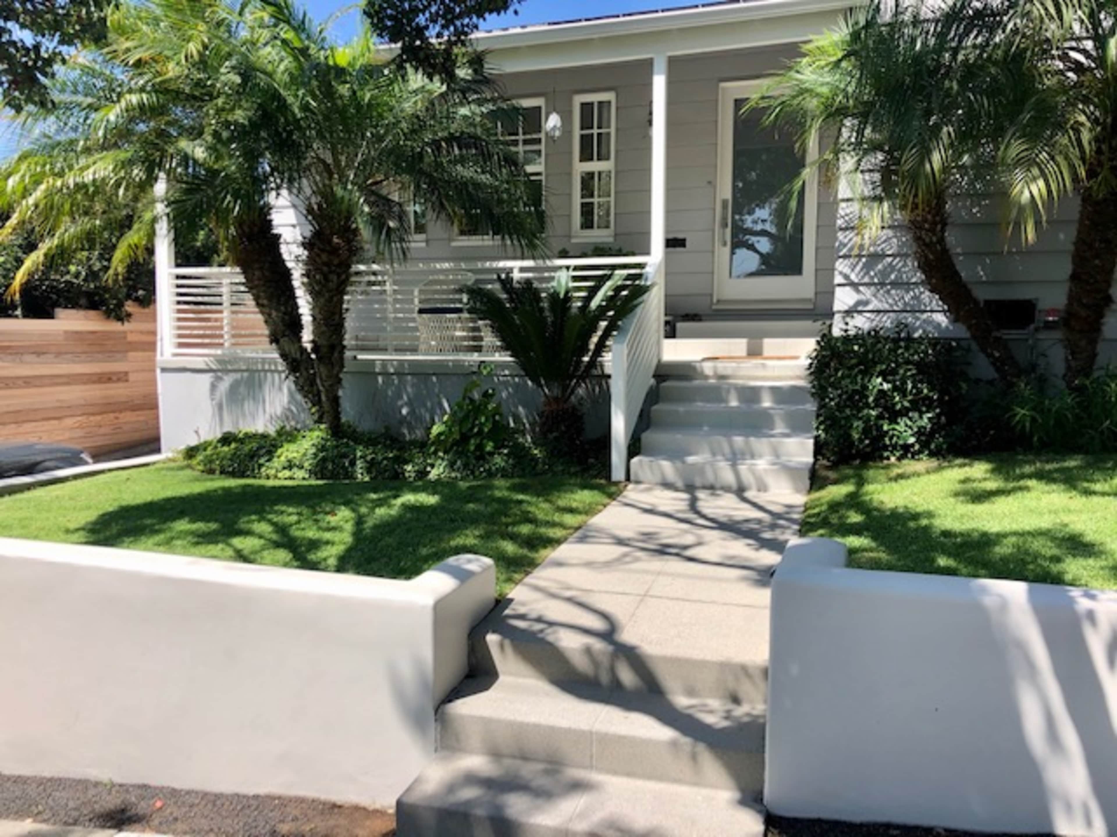 A modern house with palm trees and a stone pathway is surrounded by a well-maintained lawn.