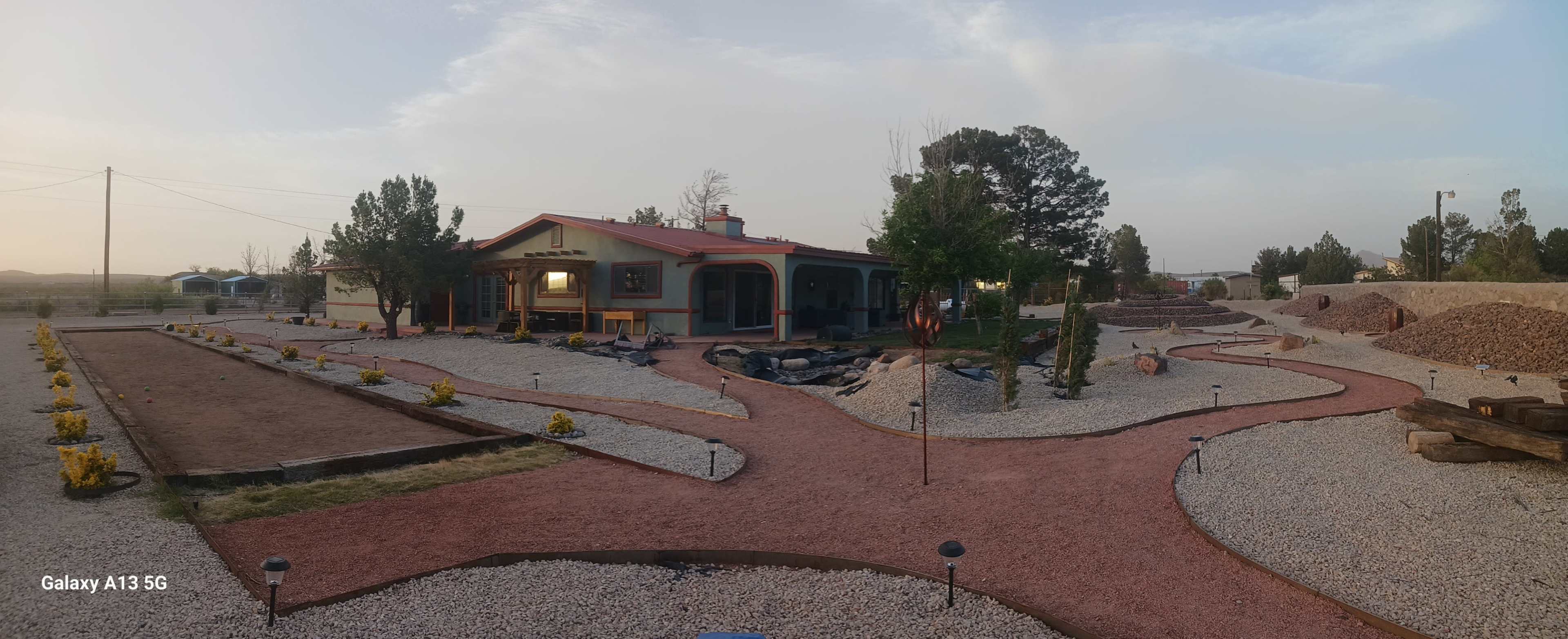 The image shows a house surrounded by a landscaped yard featuring gravel pathways, decorative plants, and outdoor lighting.