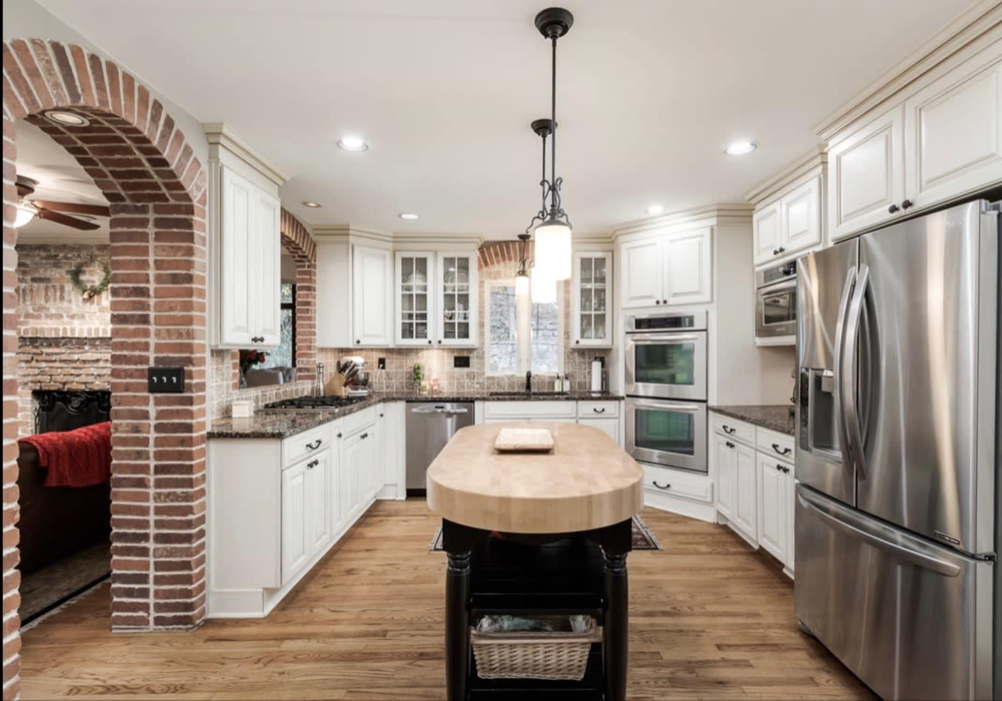 The kitchen features white cabinetry, a large wooden island, stainless steel appliances, and brick accents.