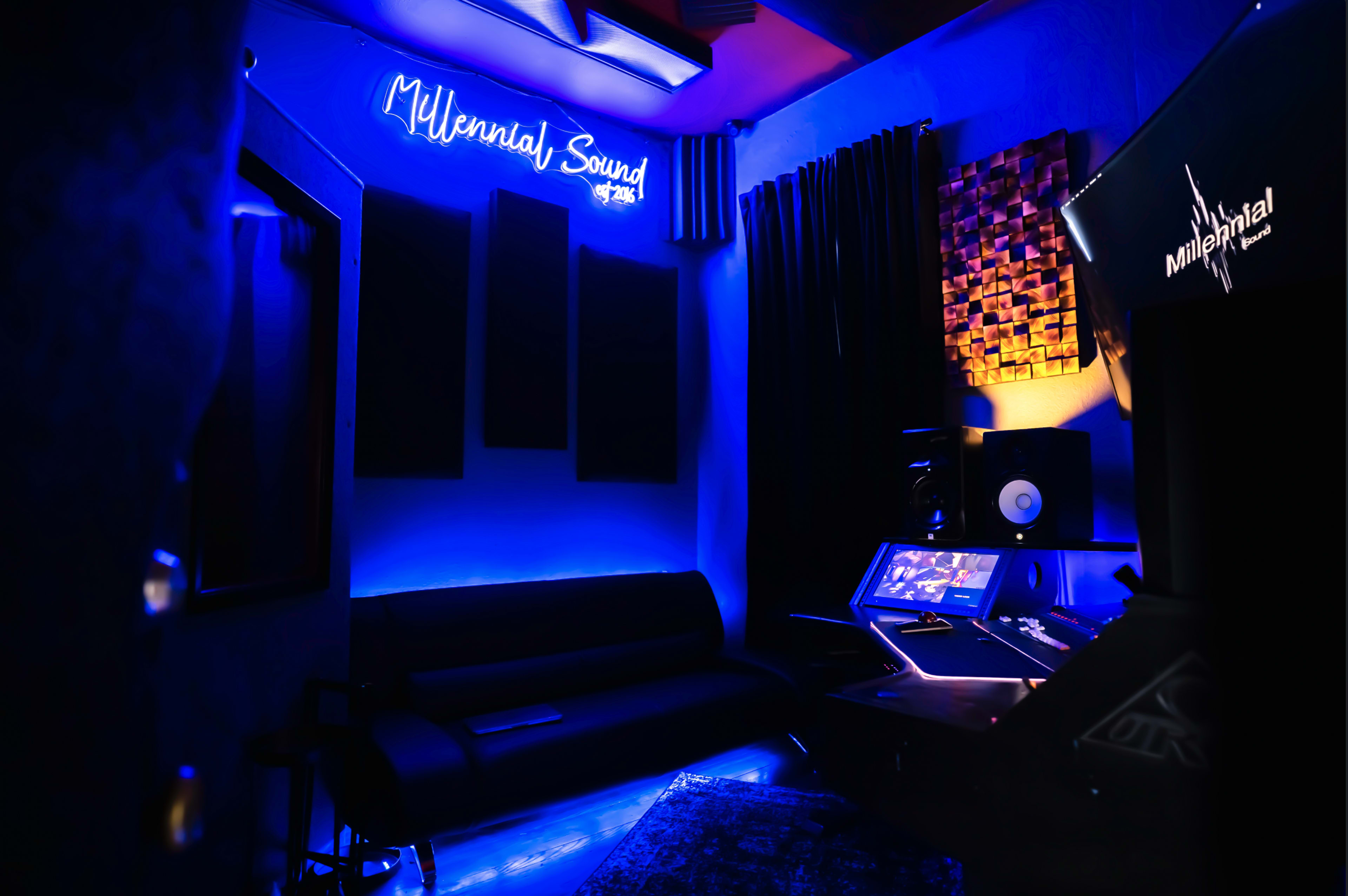 A music studio features blue lighting, a sofa, soundproof panels, and a mixing console.