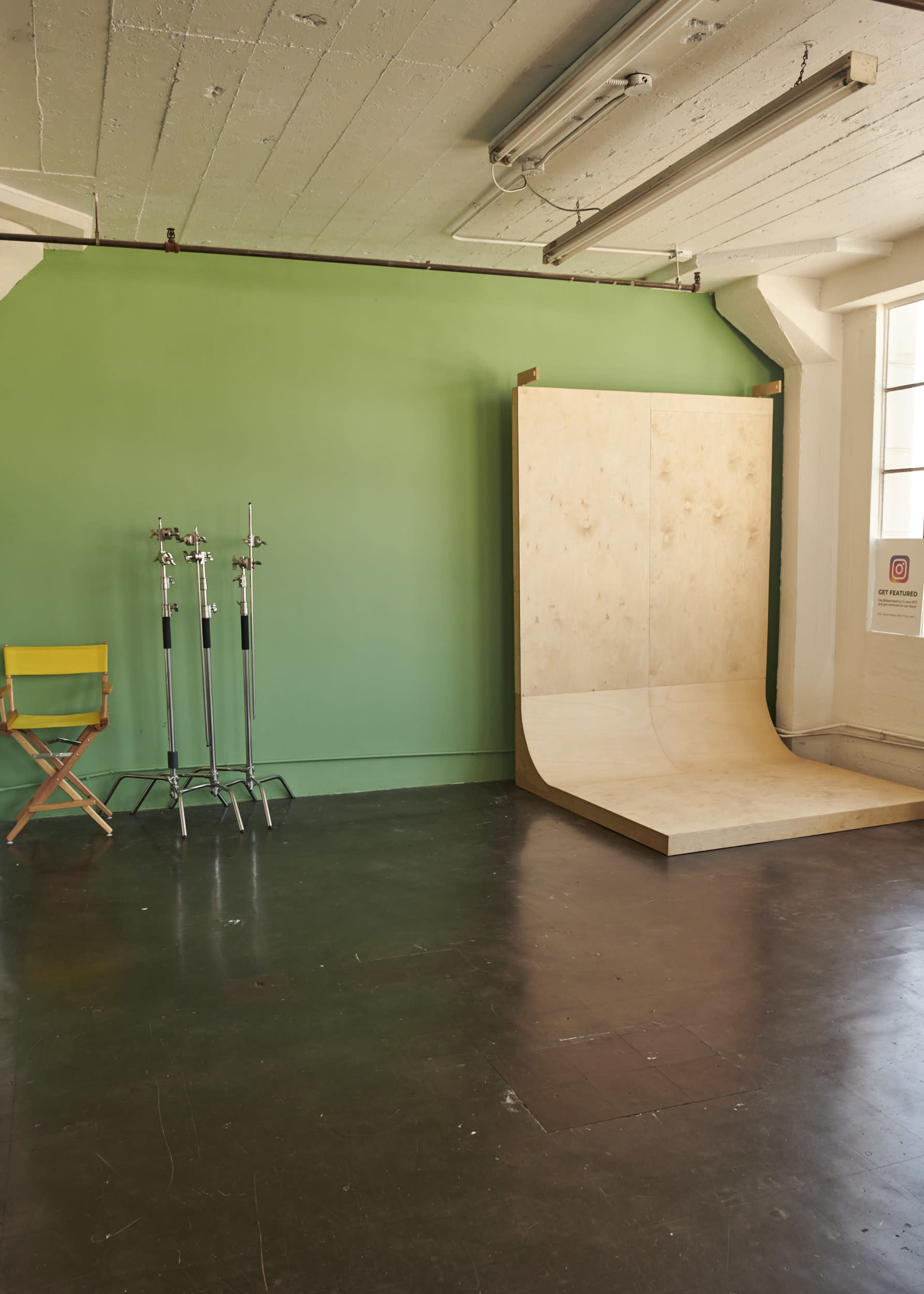 A spacious photography studio with a green backdrop, a ramp structure, and a director's chair next to several light stands.