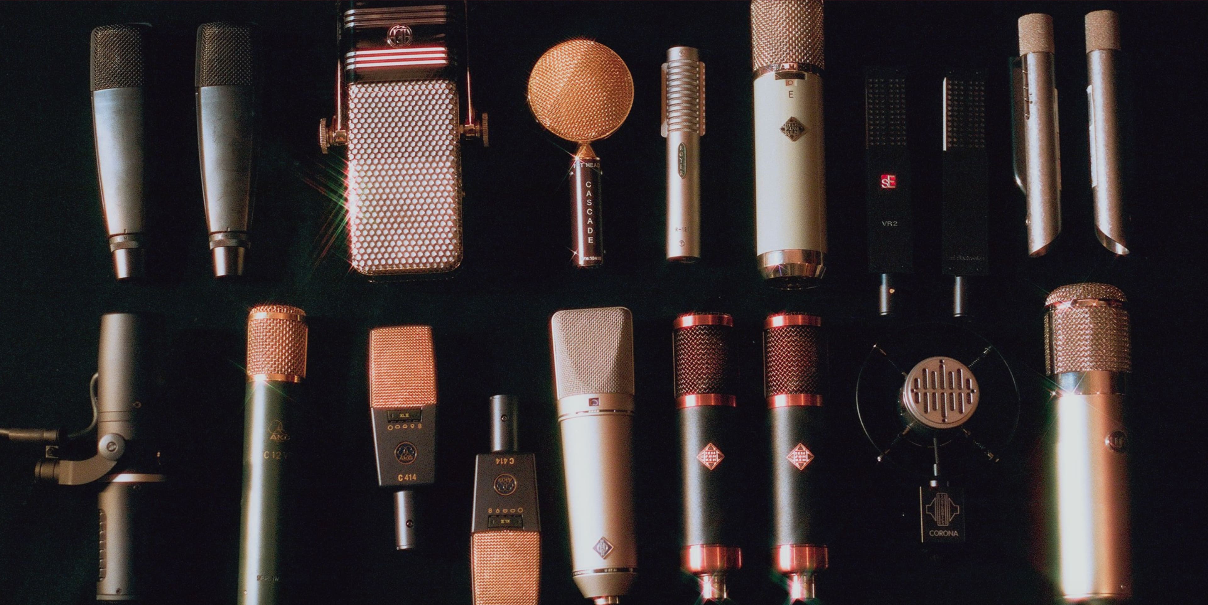 A variety of microphones are arranged in a neat grid on a dark surface.