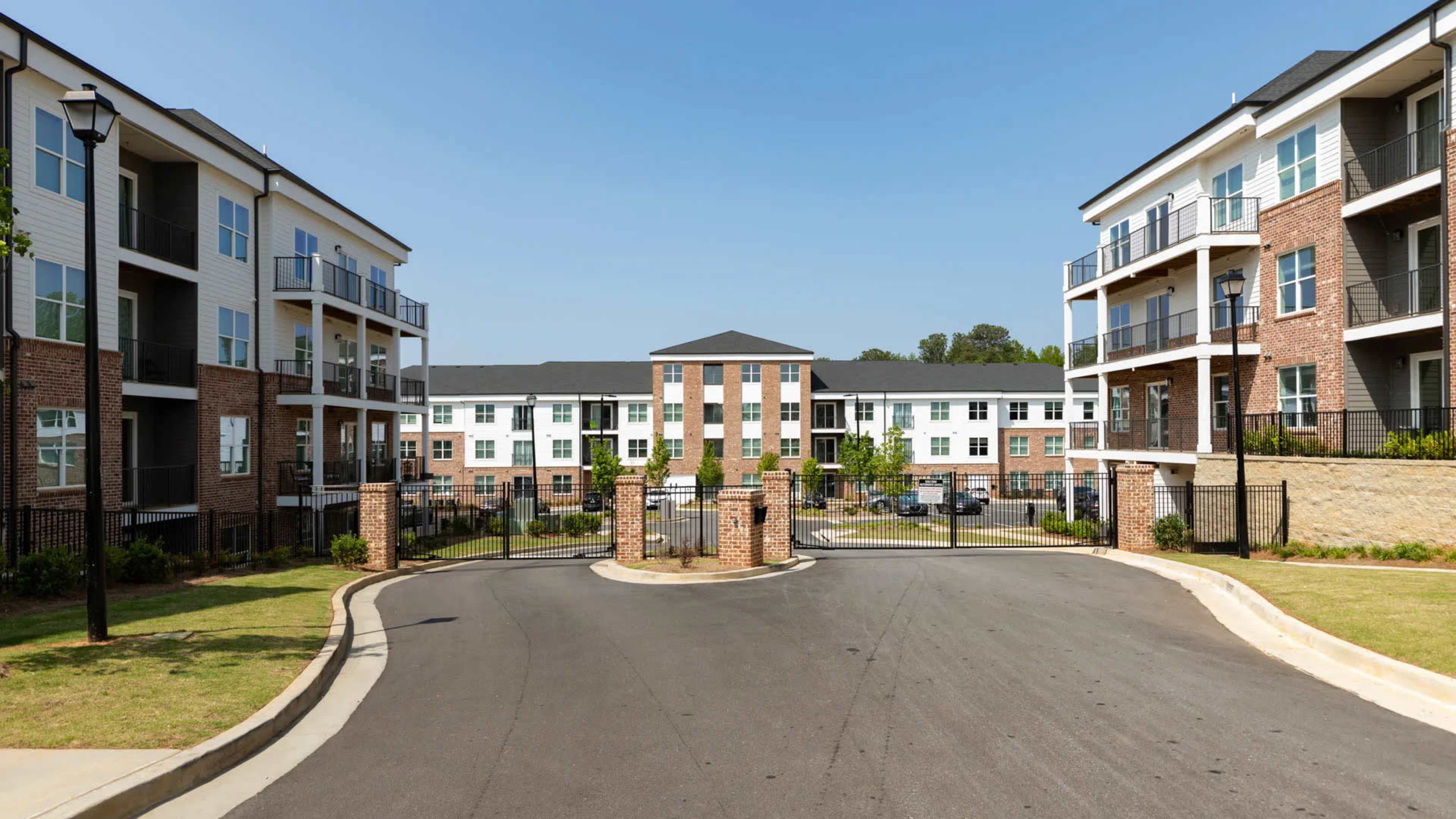 A gated residential complex with several three-story buildings and a paved roadway leading into the entrance.