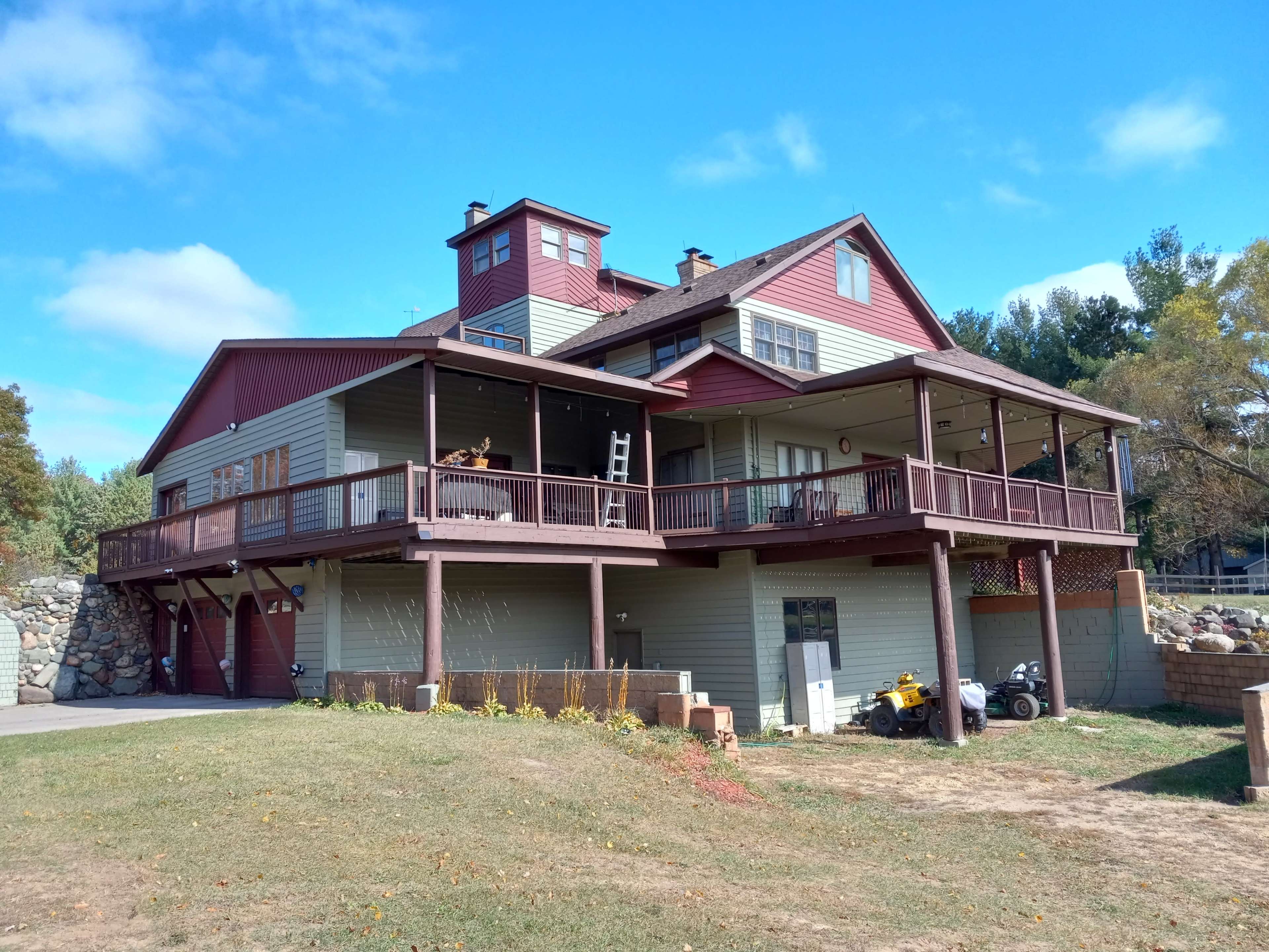 A large, multi-level house with a wraparound porch and a stone wall in the front yard.