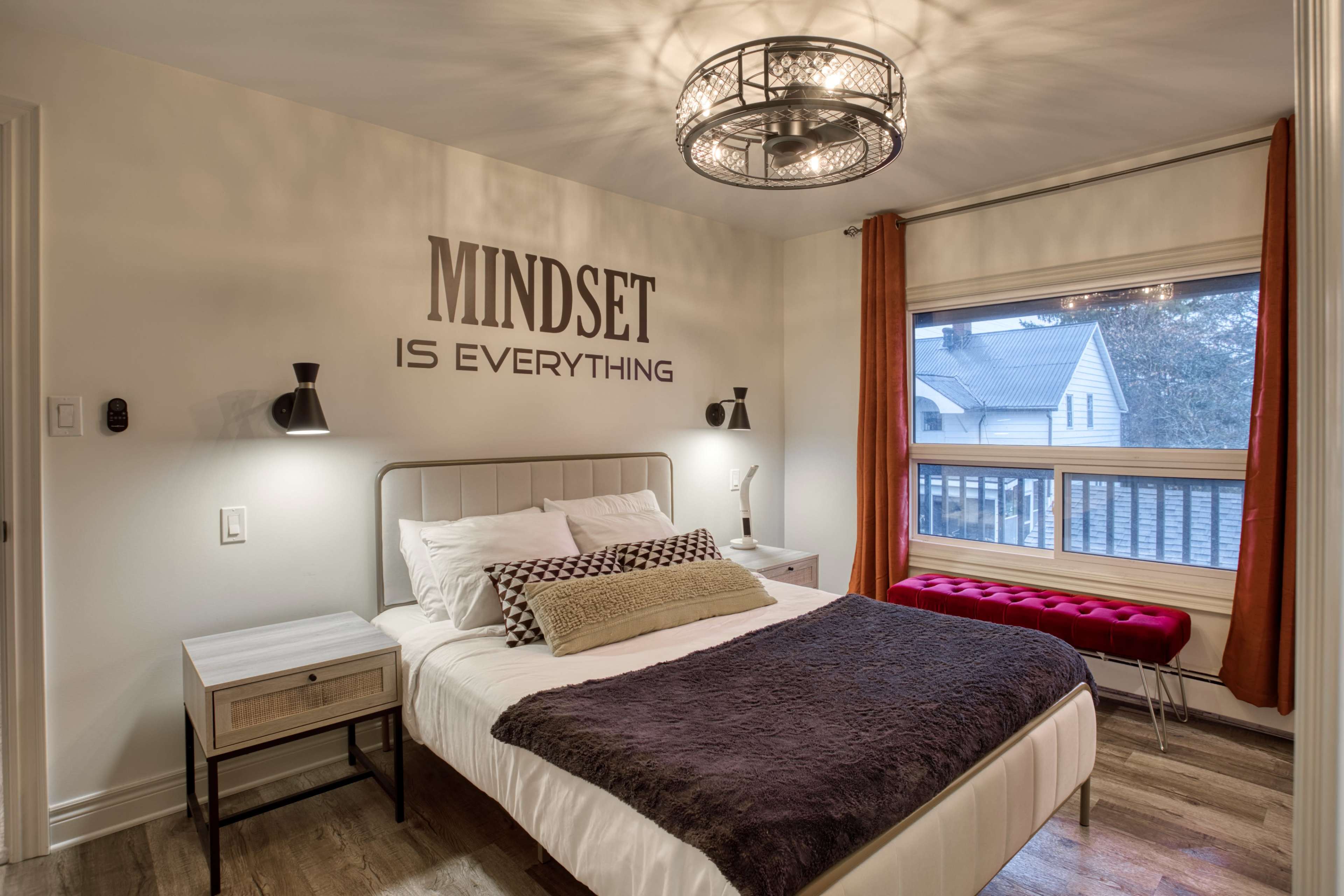 A well-decorated bedroom features a bed with a dark throw blanket, accented by a stylish light fixture and motivational text on the wall.