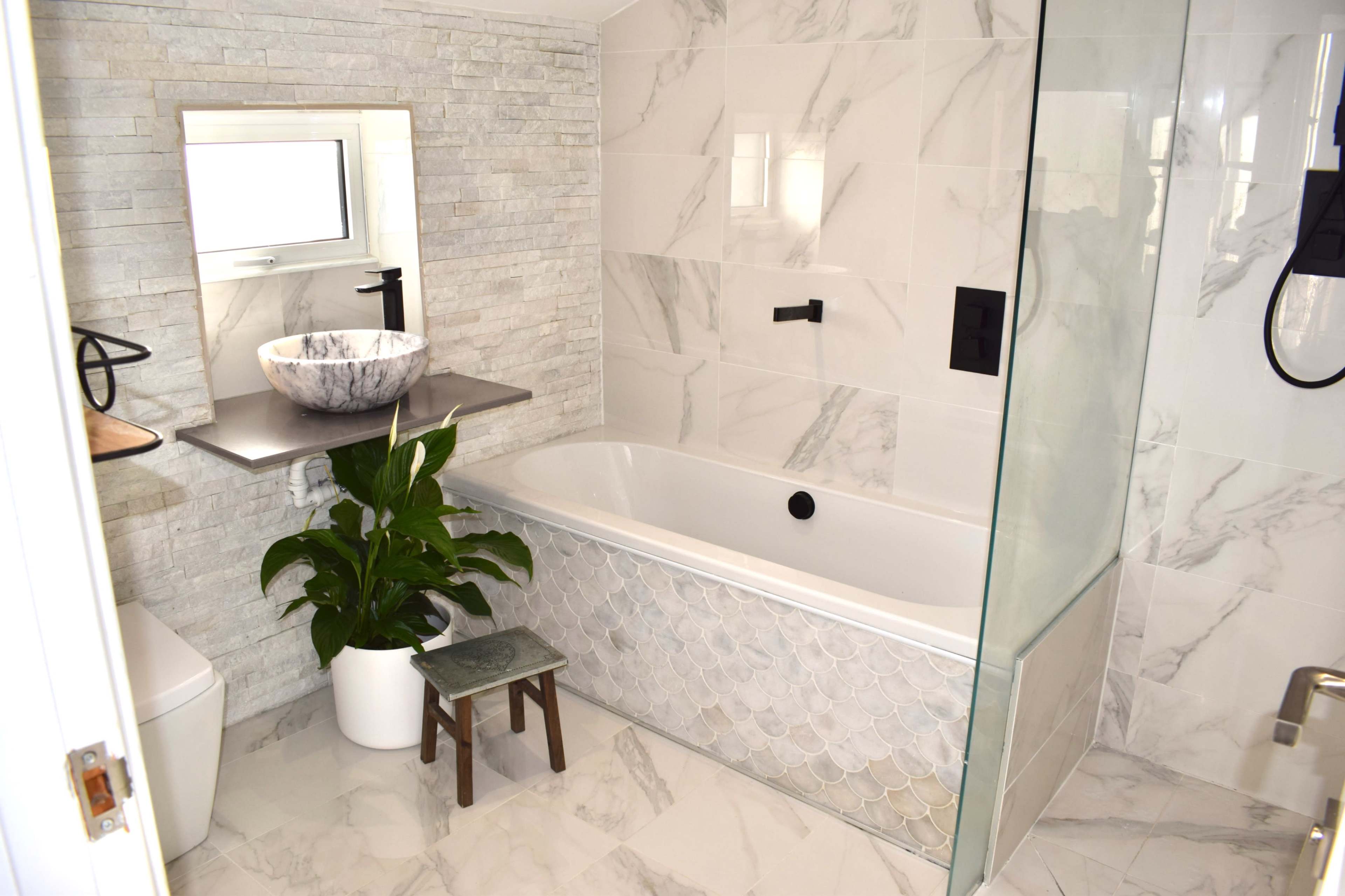 A modern bathroom featuring a freestanding bathtub, a stone sink on a floating shelf, and a potted plant beside a toilet.