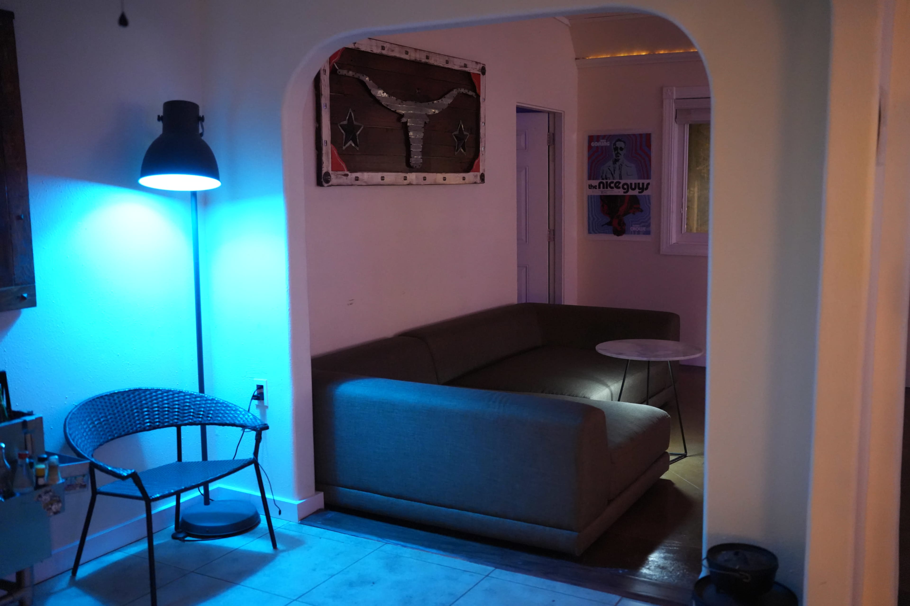 The image shows a modern living space with a gray couch, a round table, and a black chair illuminated by a blue lamp.