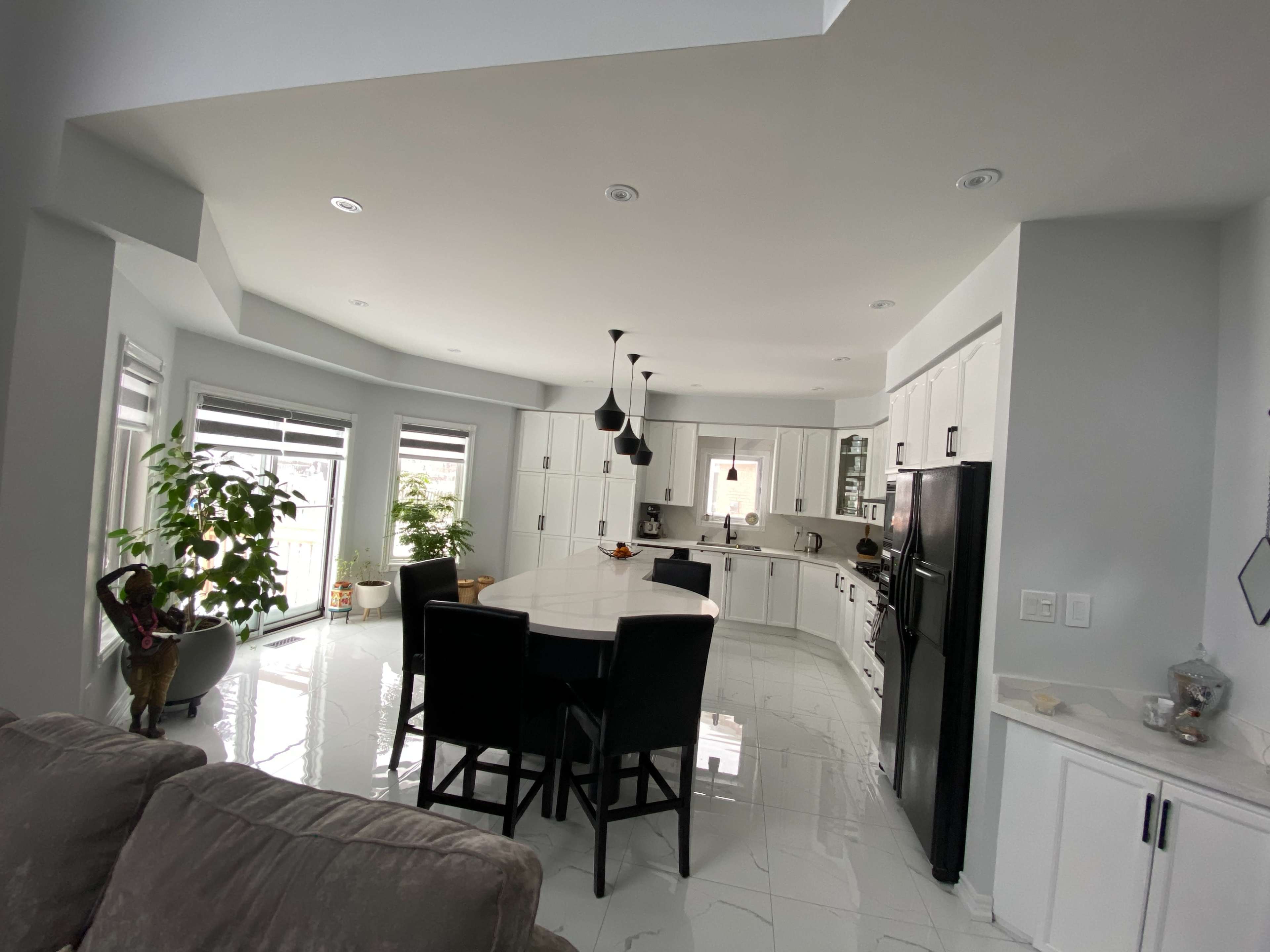 A modern kitchen features white cabinetry, a large island with seating, and black appliances, illuminated by pendant lights.
