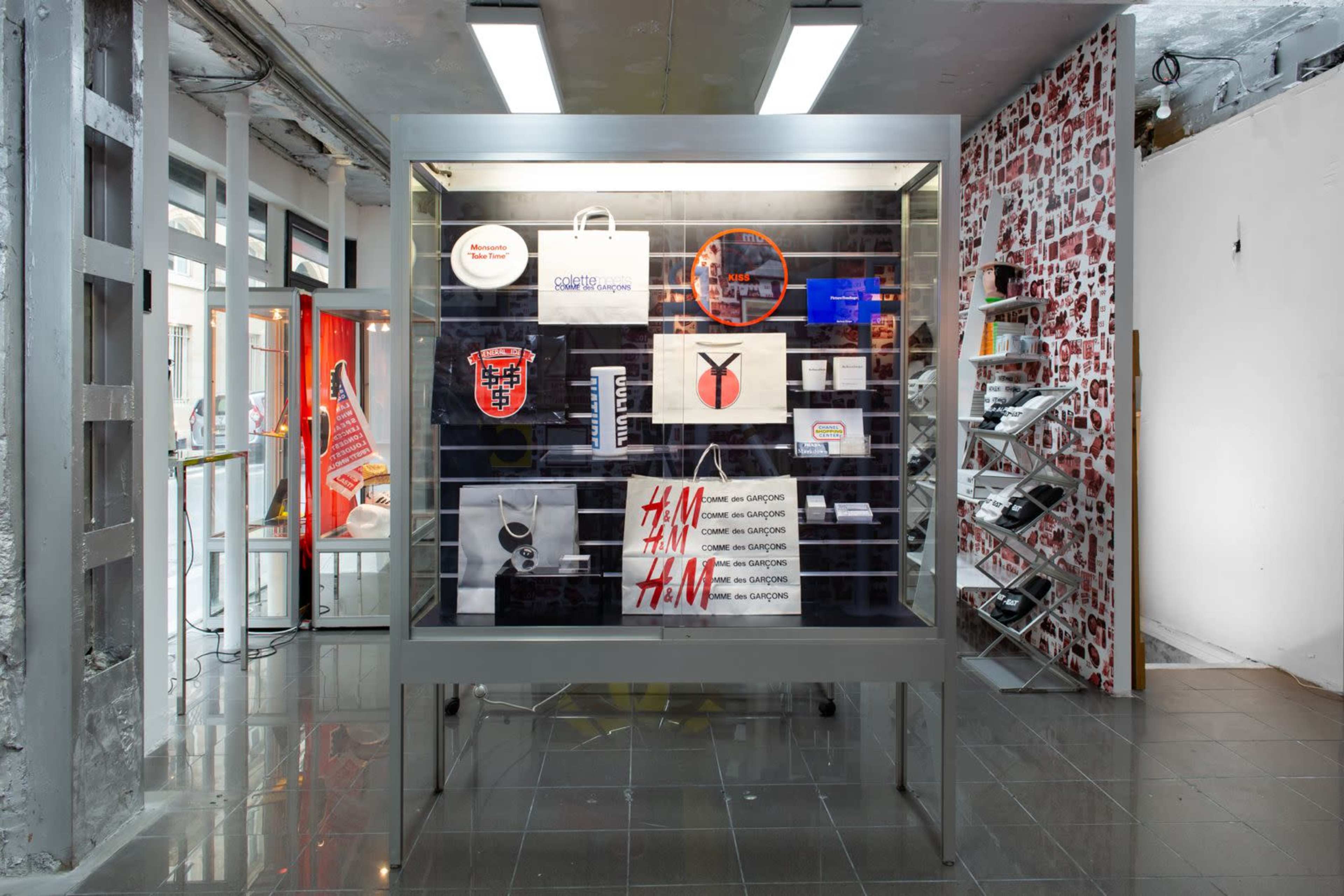 The image shows a display case featuring various creative items, including bags, posters, and graphic designs, within a contemporary retail space.