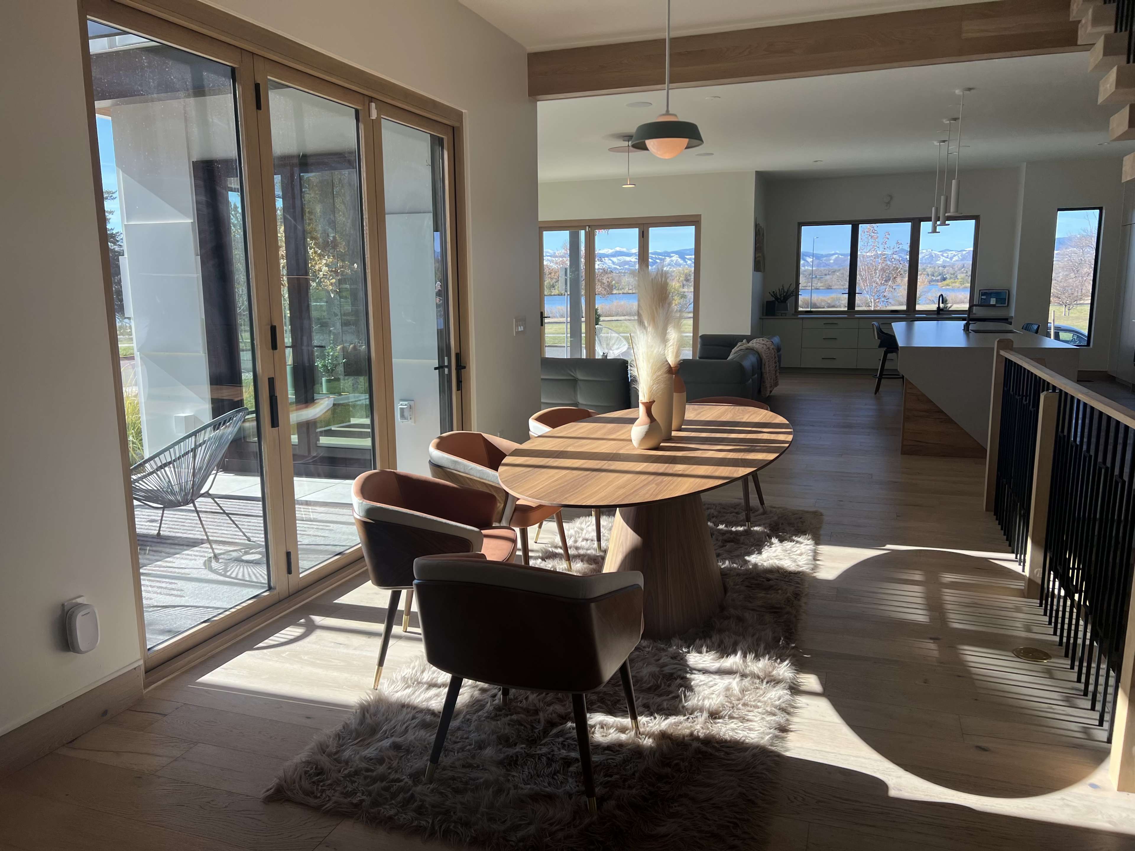 A dining area features a round table surrounded by chairs, with large windows showcasing a view of the outdoors.