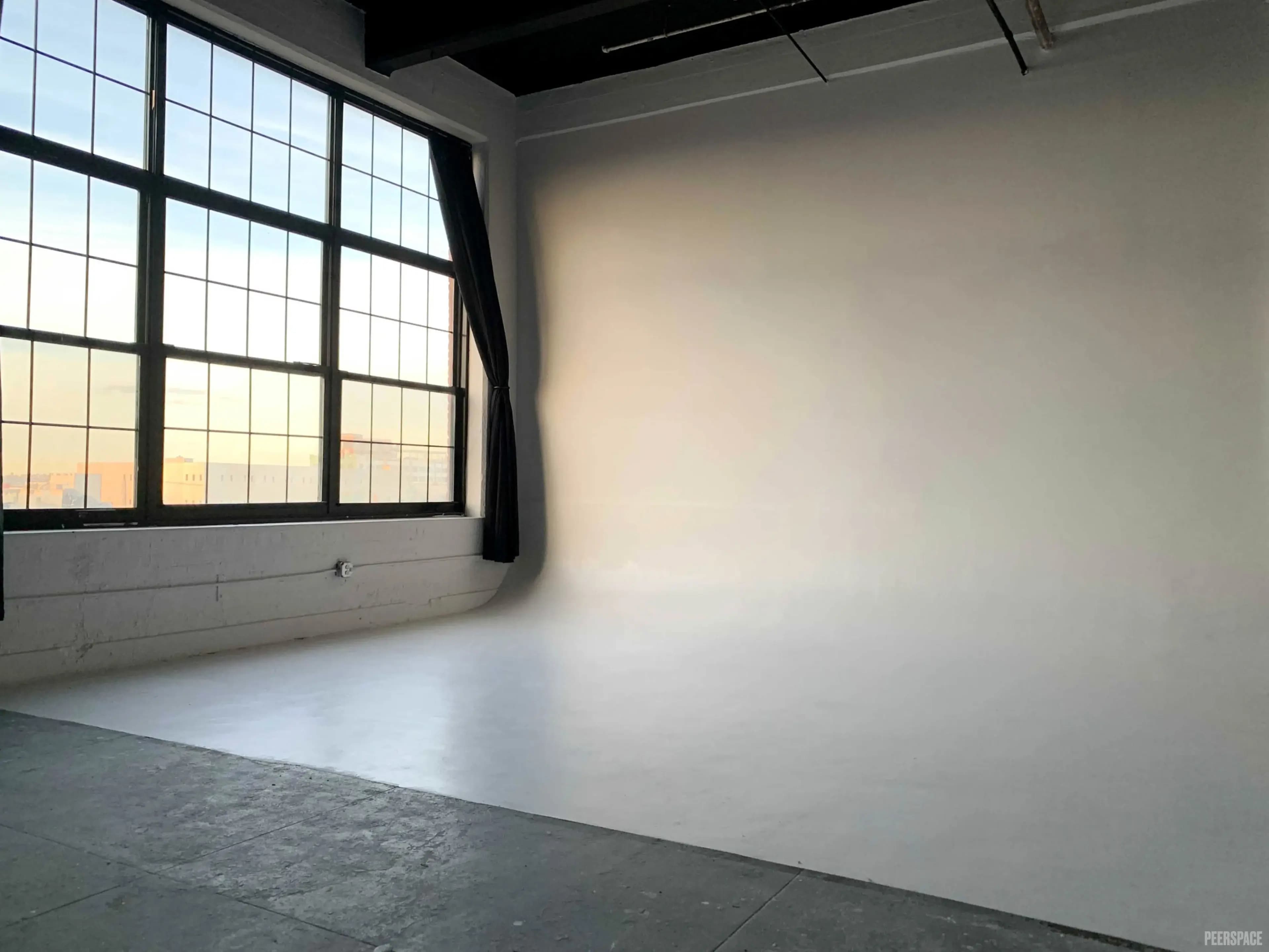The image shows a spacious photography studio with large windows and a plain white backdrop.
