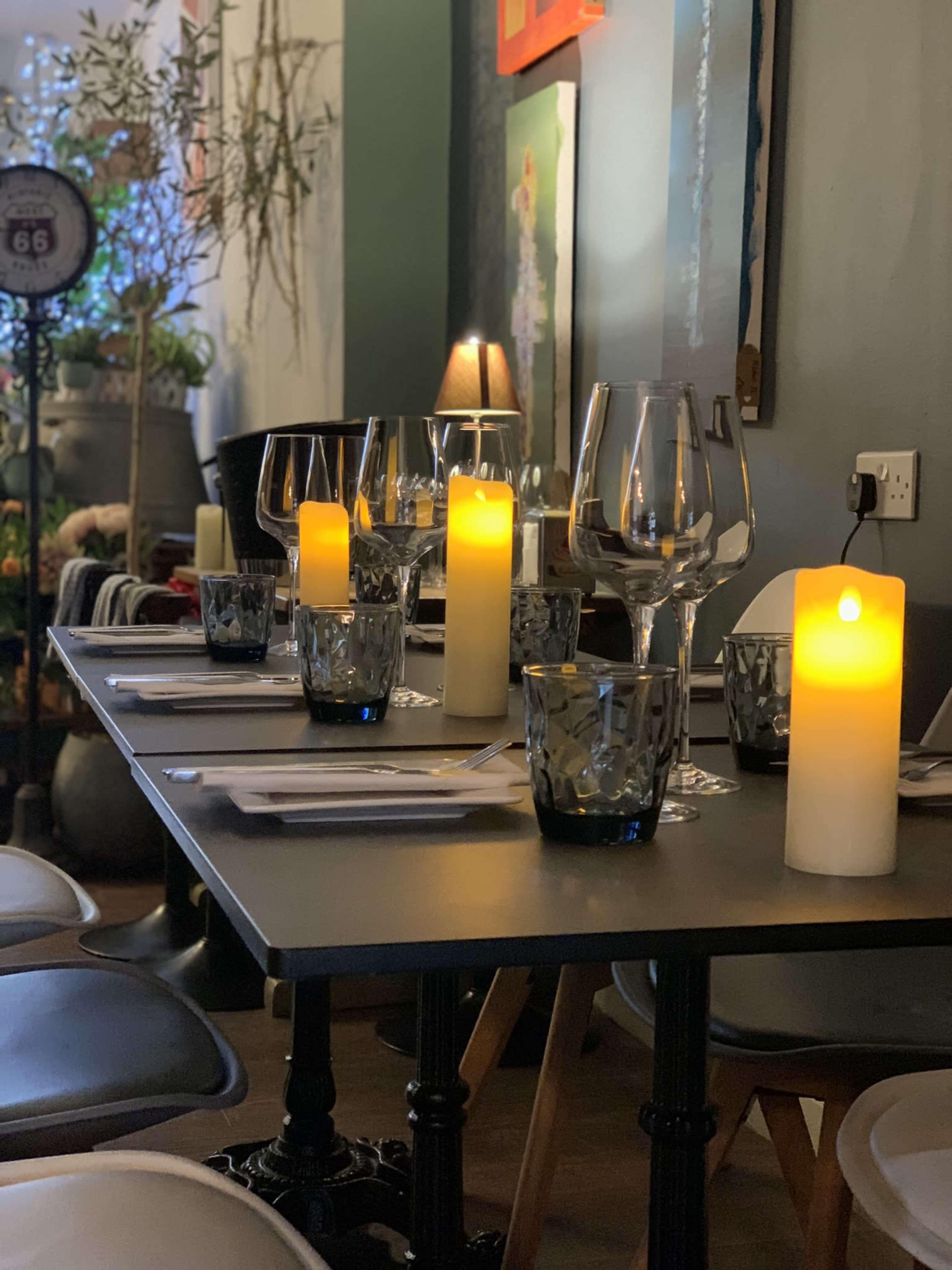 ADining table is set with glasses, candle holders, and illuminated candles in a cozy room.
