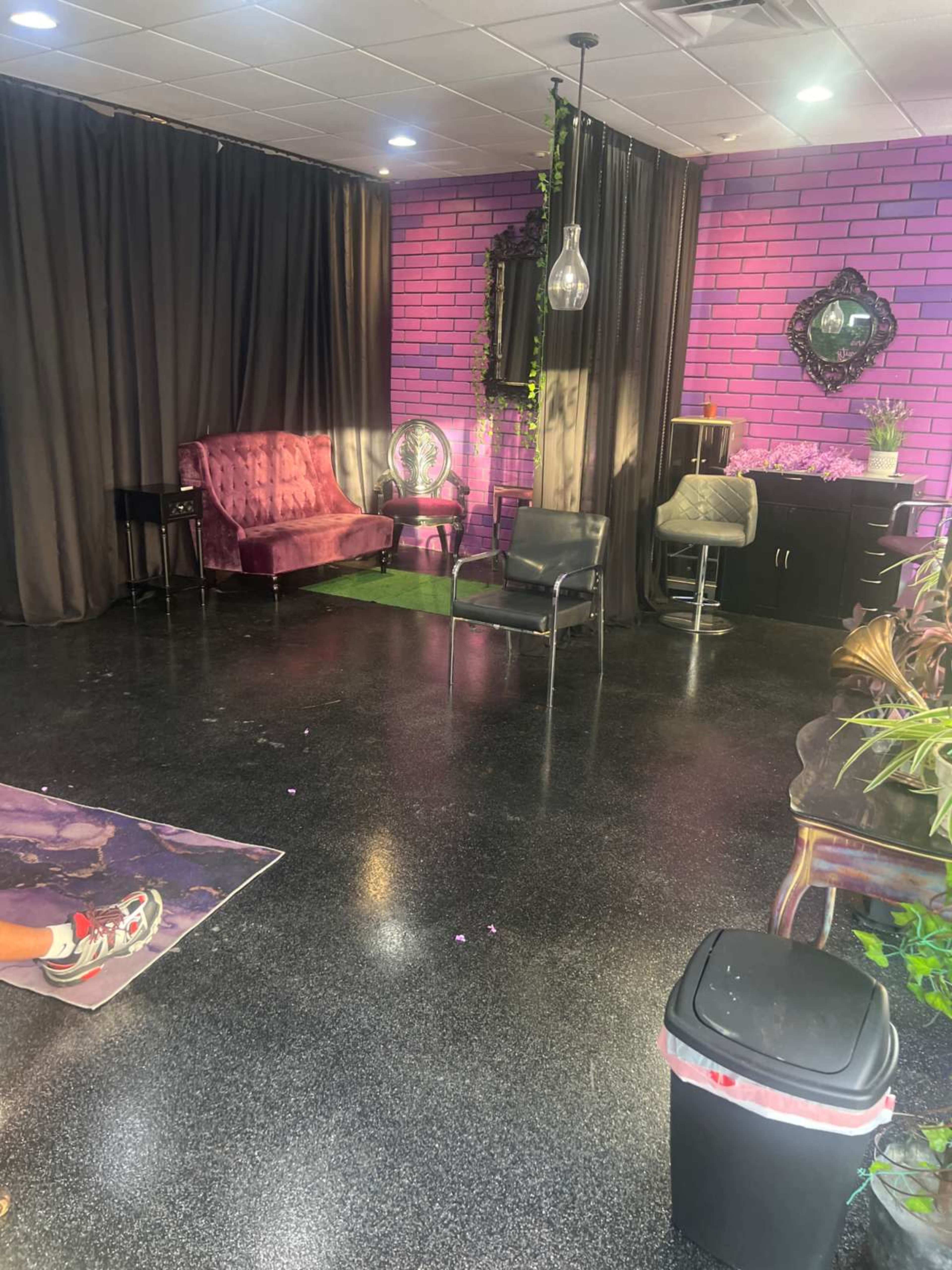 The image shows a stylish interior space with pink brick walls, black curtains, and various seating arrangements.