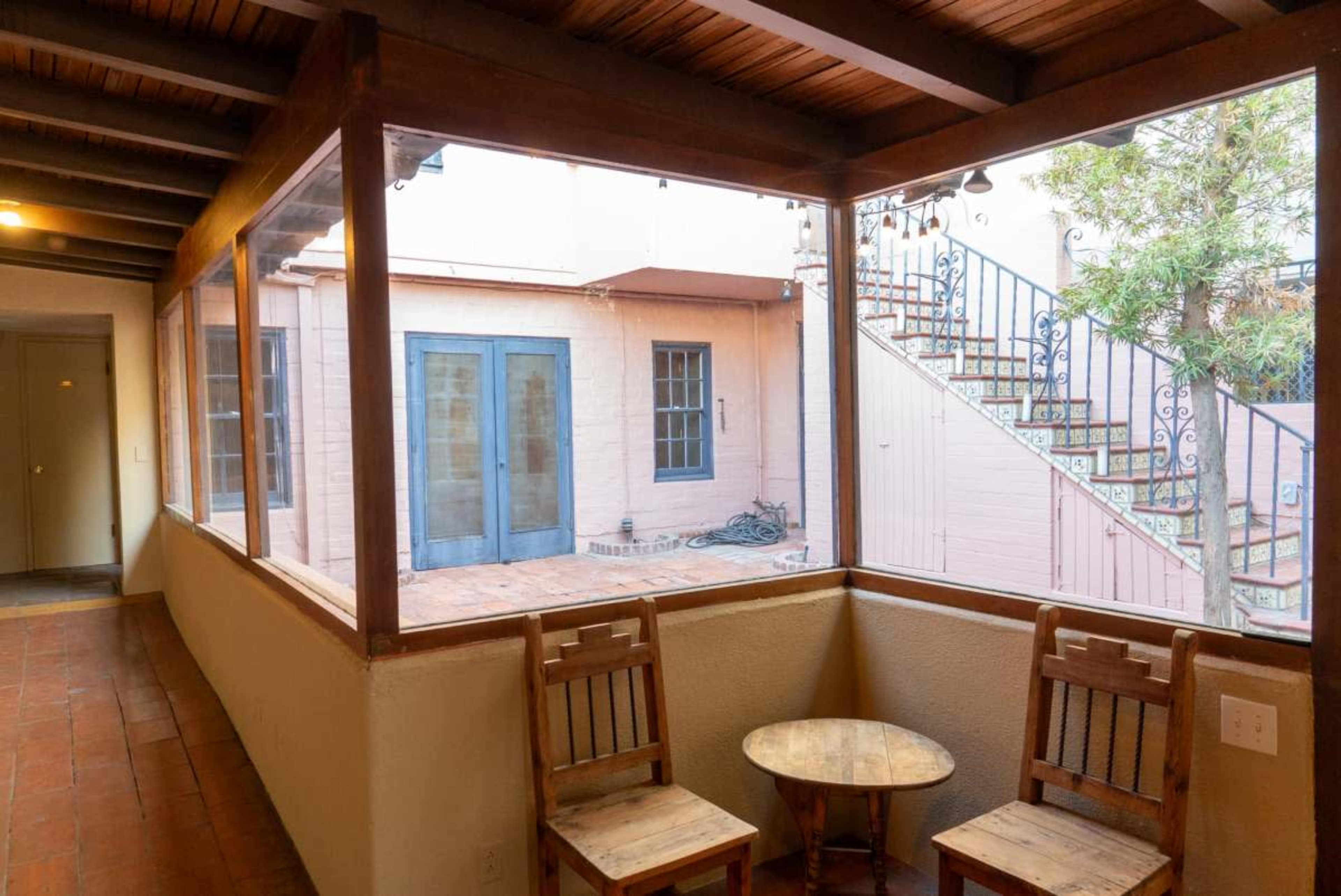The image shows a hallway with wooden chairs and a small table, leading to an outdoor area with stairs and a courtyard.