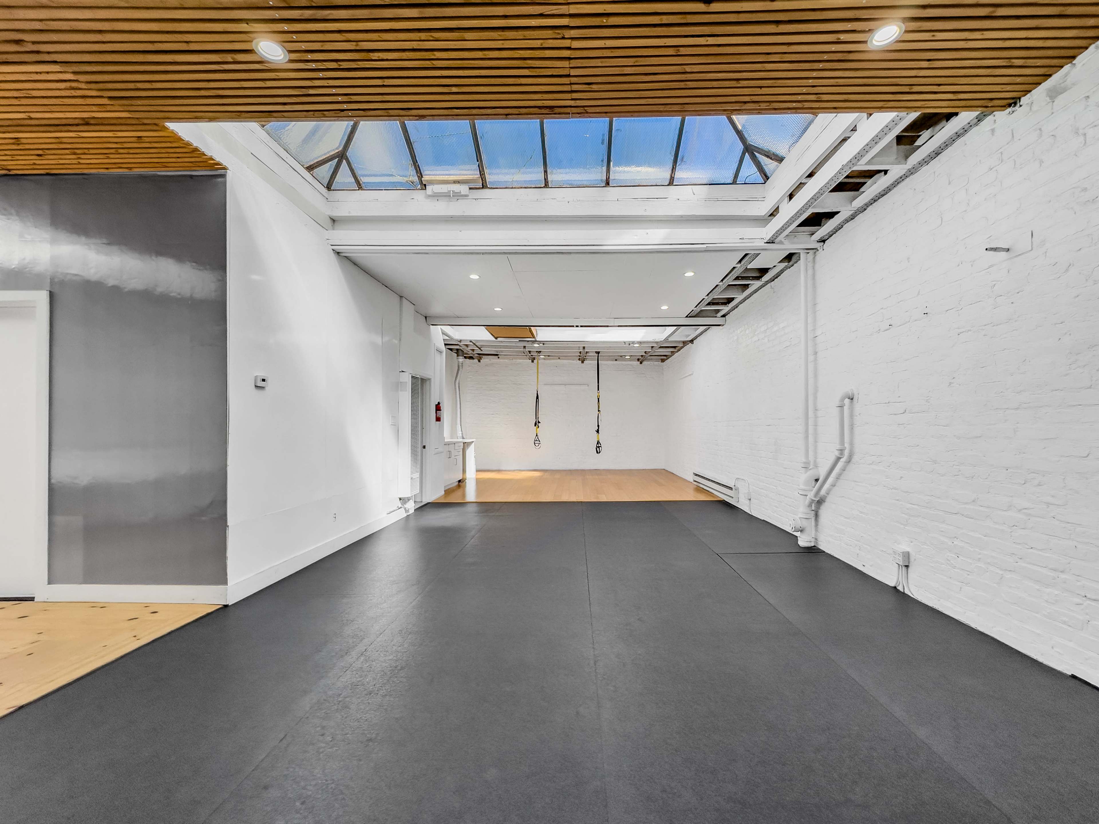 A spacious, well-lit interior room with wooden beams and a black rubber floor.