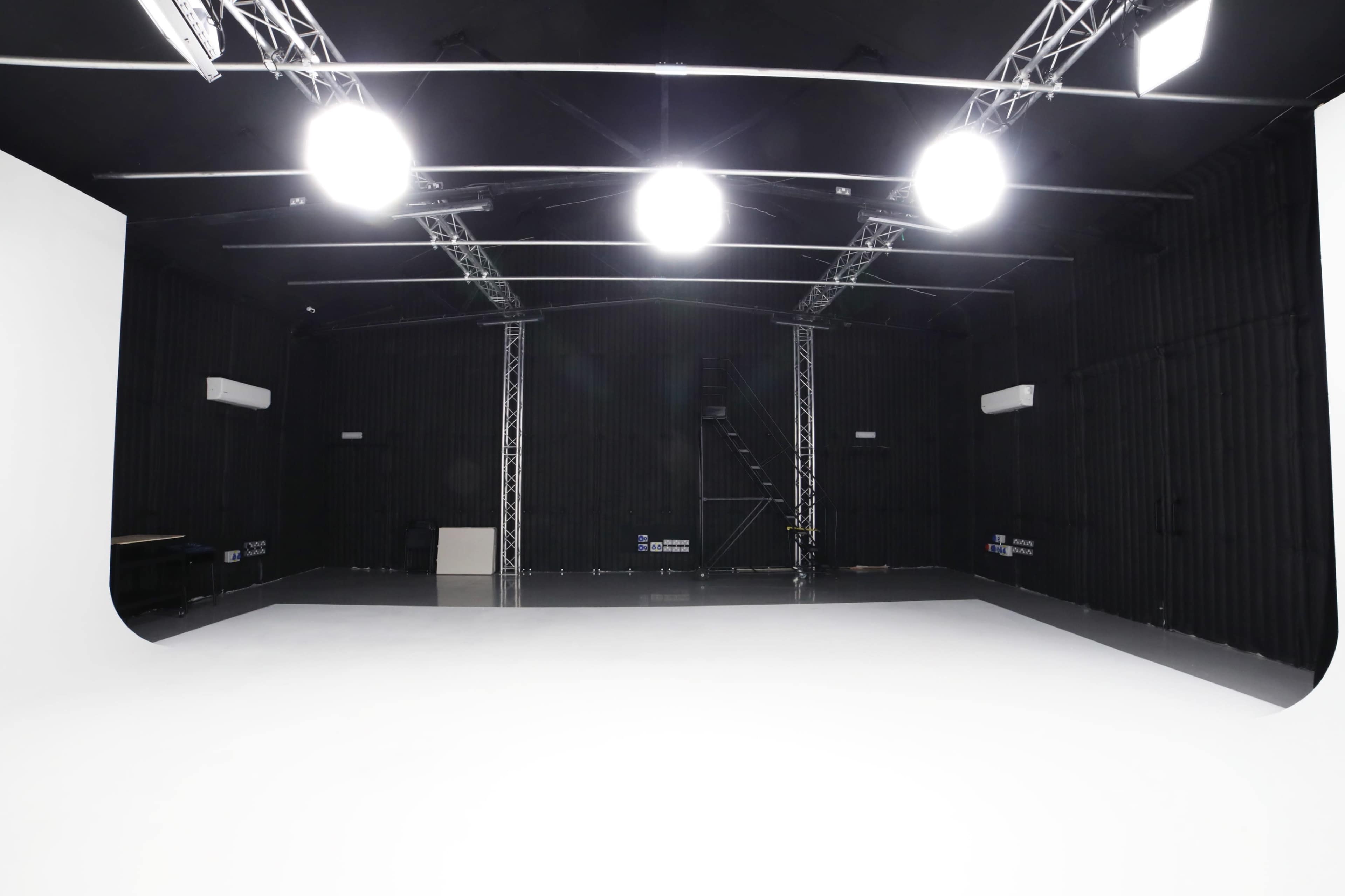 An empty studio space with a white backdrop, overhead lights, and black walls.