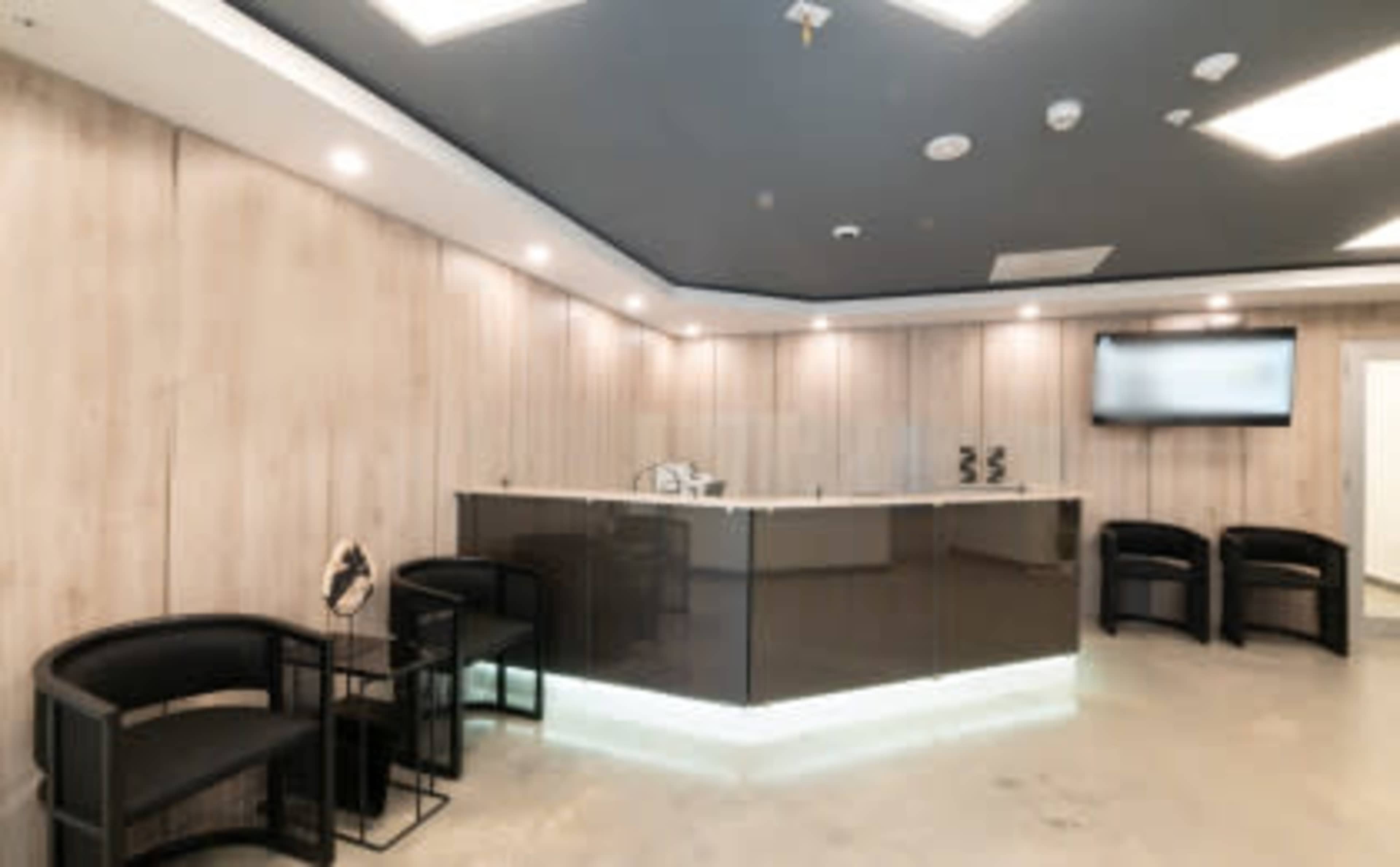 A modern reception area features a sleek front desk with dark materials and minimalist seating arrangements against a light wood panel backdrop.