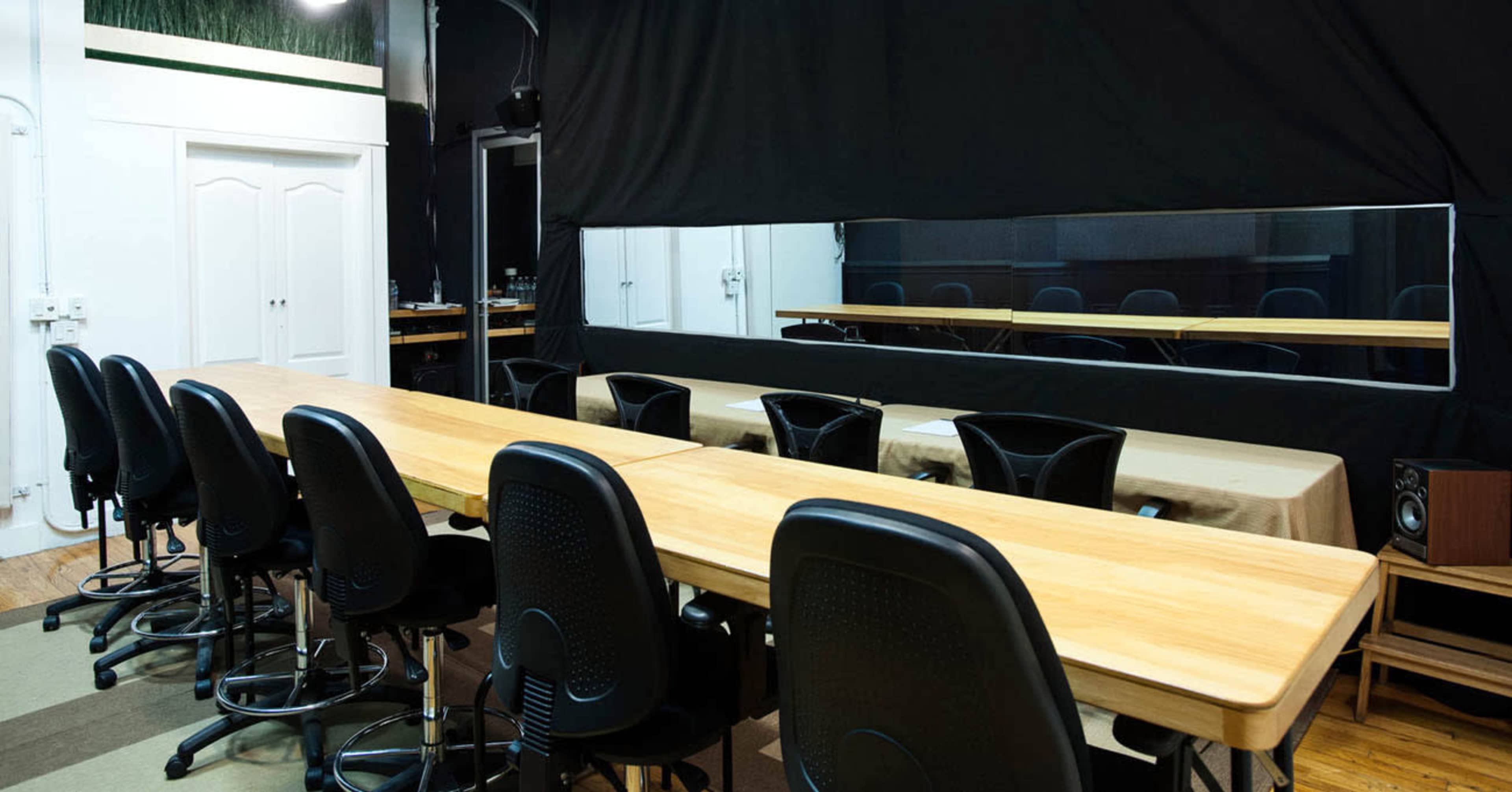 A long wooden table with black rolling chairs is set up in a room that features a large mirror and a curtain backdrop.