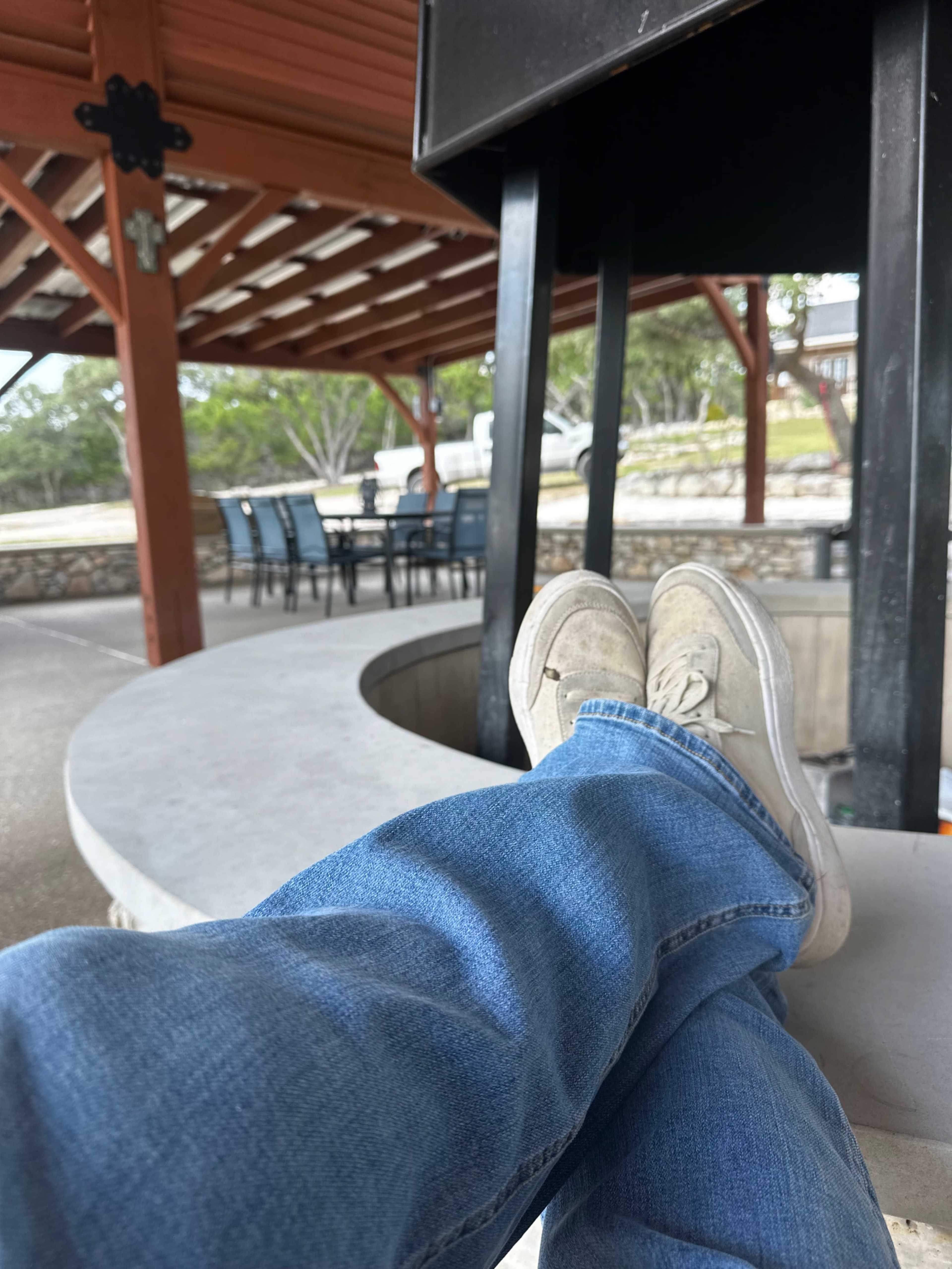 A person is sitting with their feet up on a stone gazebo ledge, with outdoor seating visible in the background.