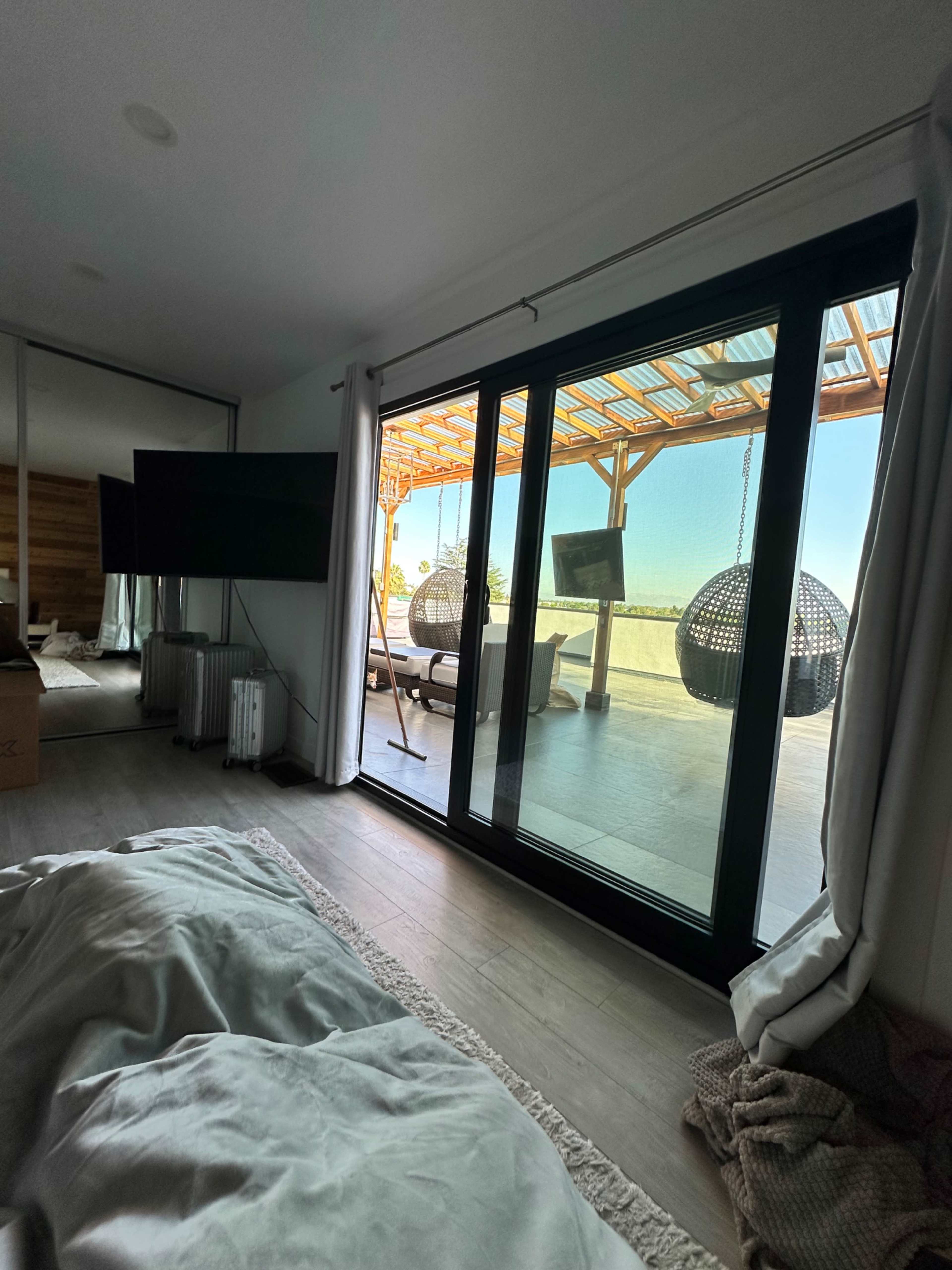 A bedroom with a bed in the foreground, large glass doors leading to a patio with hanging chairs and a view of the outdoors.