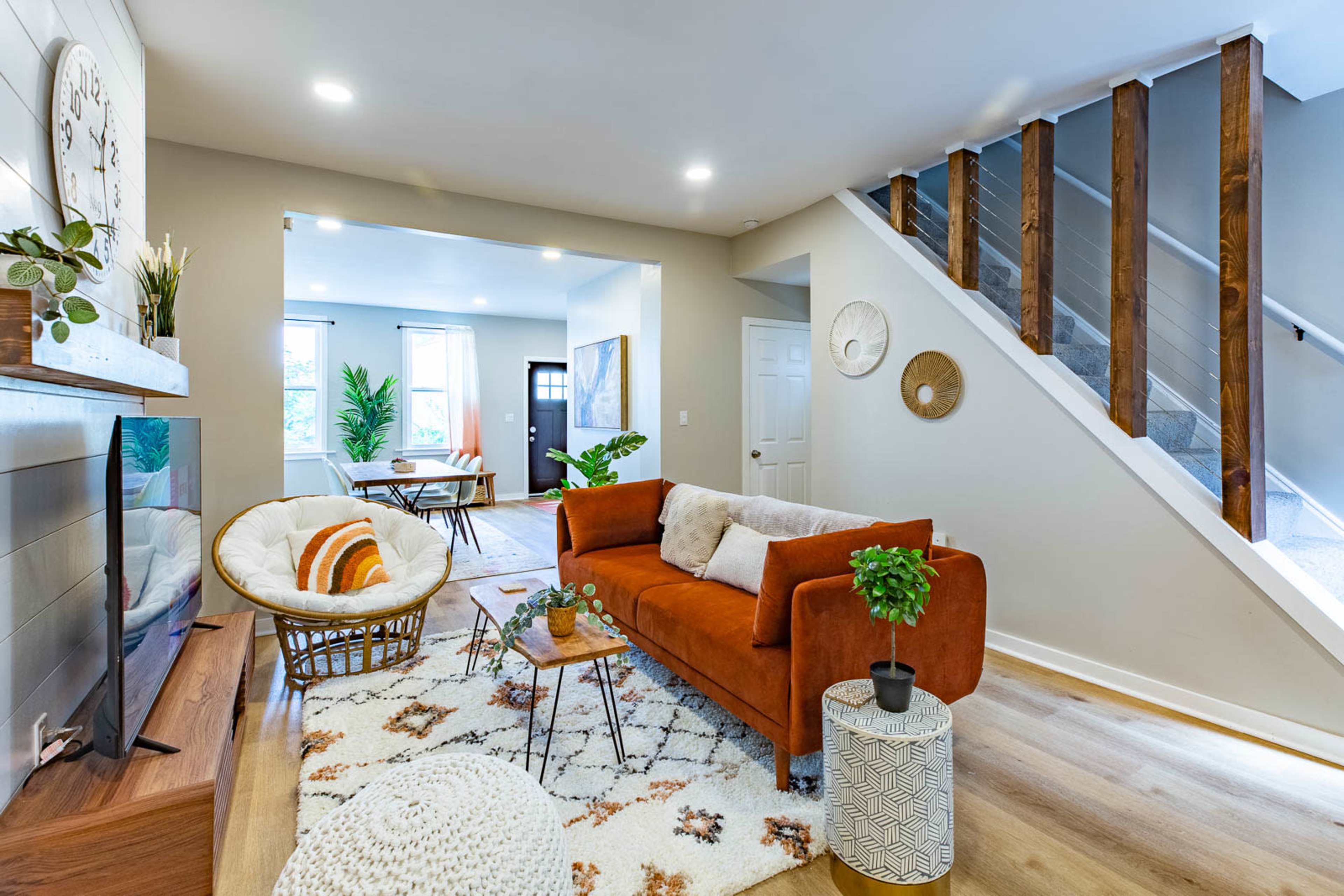 A modern living room with an orange sofa, a patterned rug, a round coffee table, and a staircase leading to an upper level.