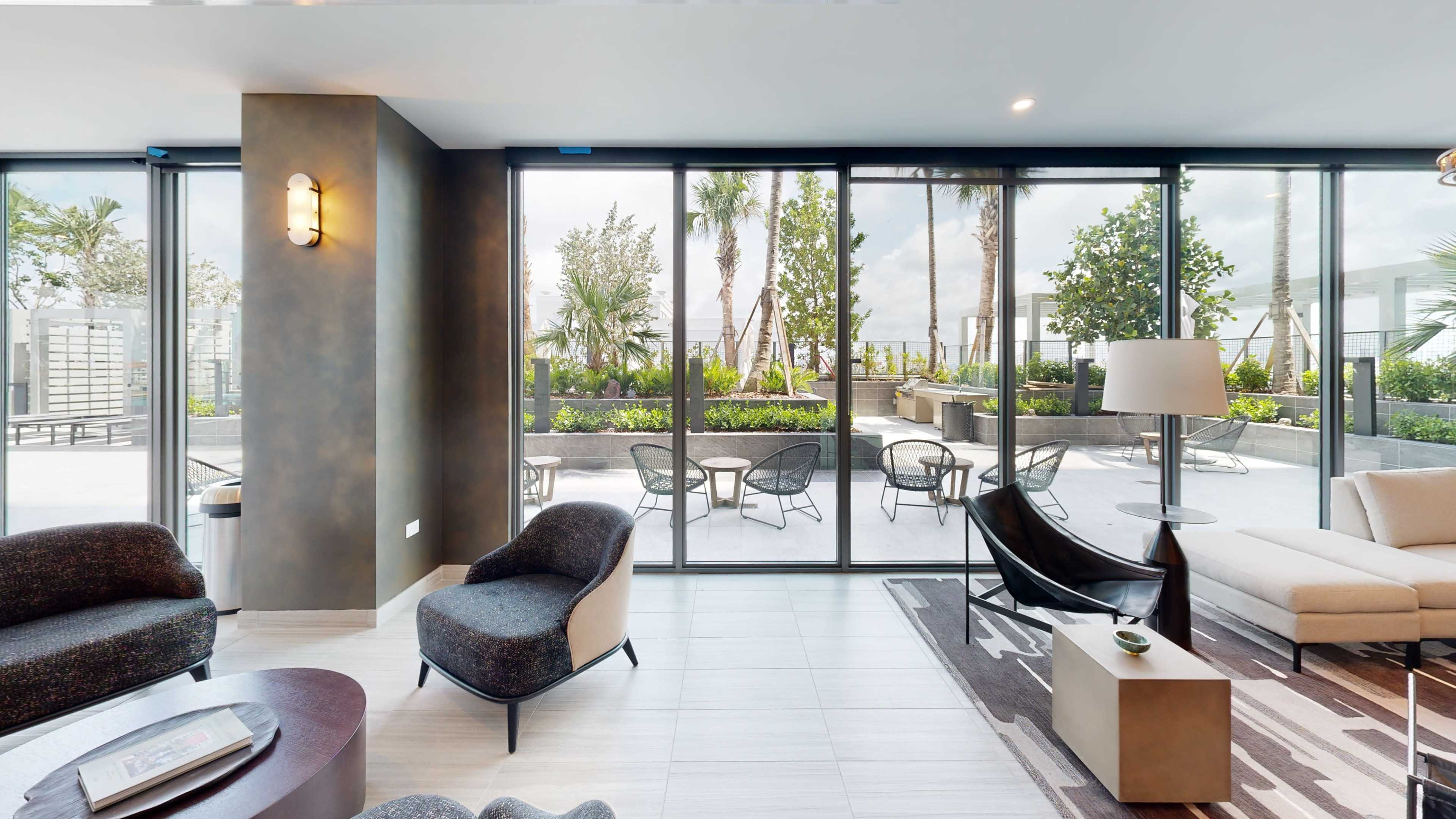 A modern lounge area features large glass doors opening to a landscaped outdoor patio with seating.