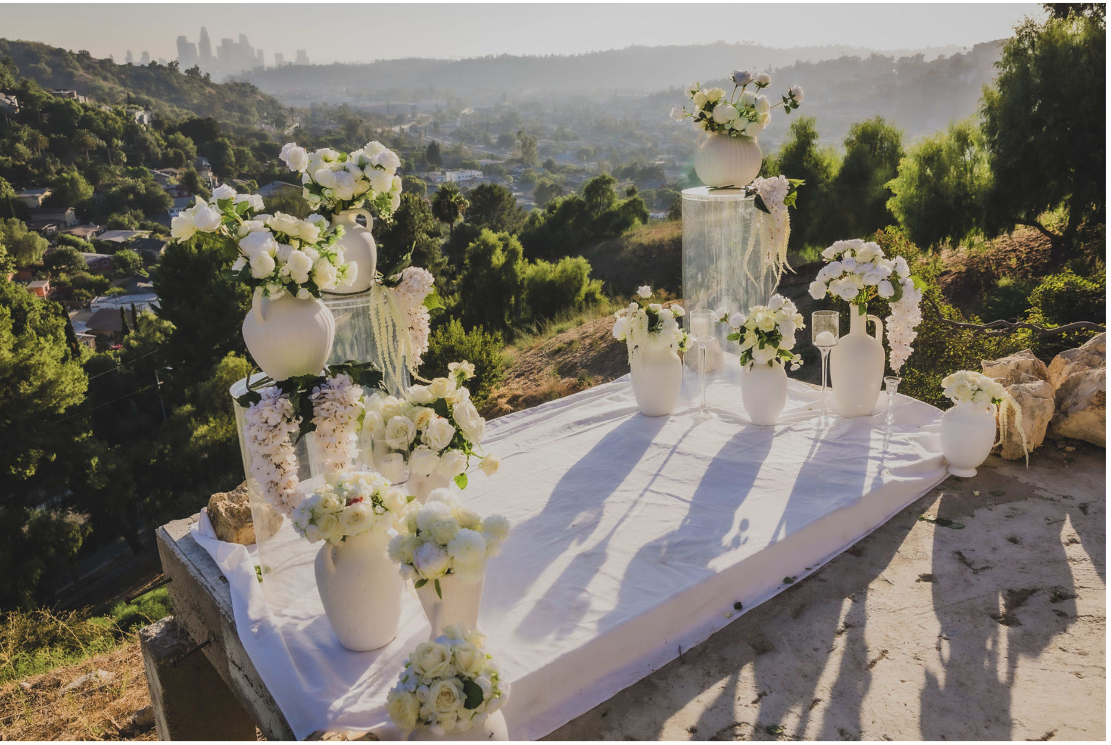 A decorated wedding altar featuring white flowers and vases is positioned on an elevated platform with a city skyline in the background.