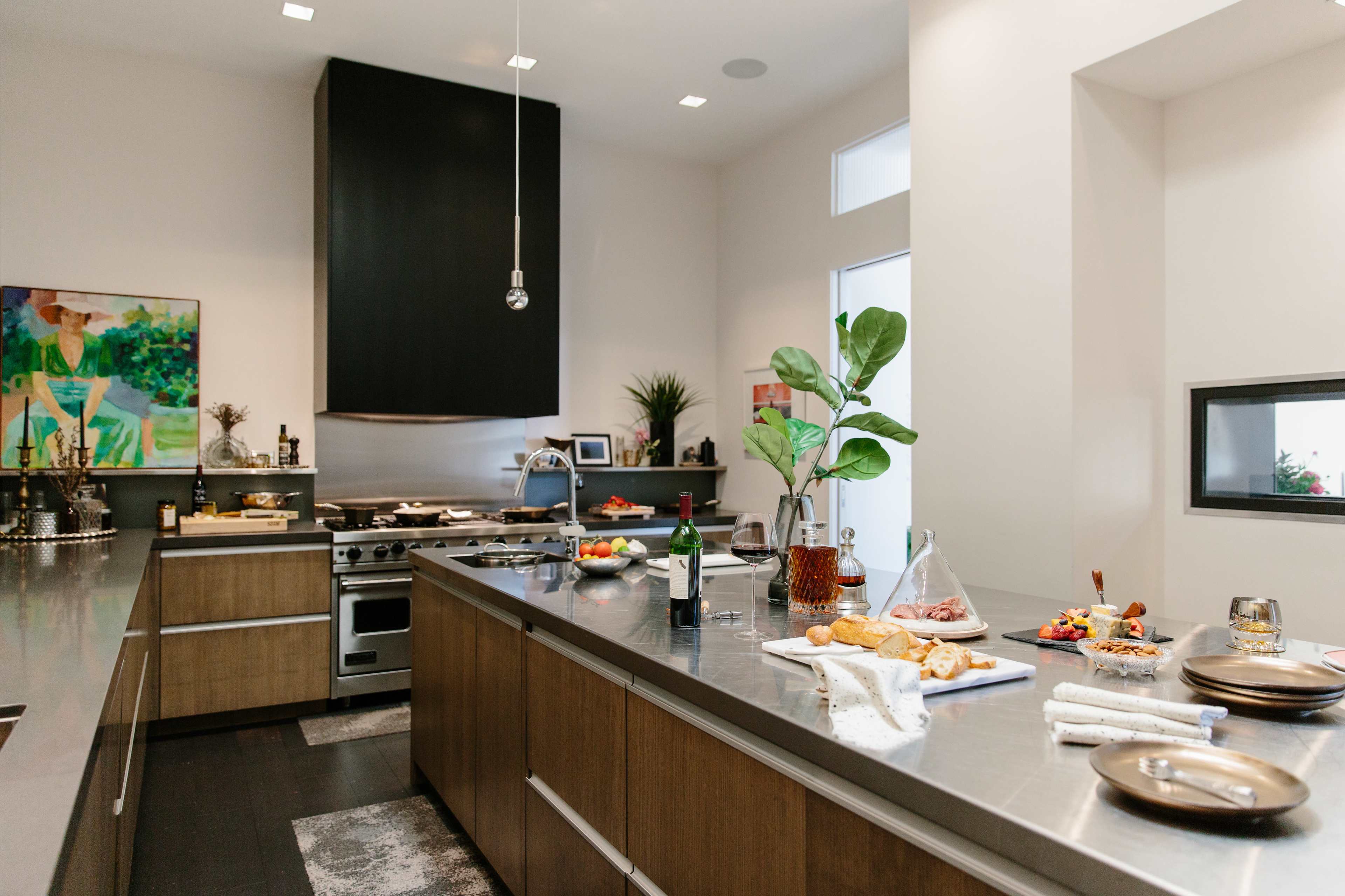 A modern kitchen features stainless steel countertops, wooden cabinets, and a variety of food and drink items displayed on the central island.