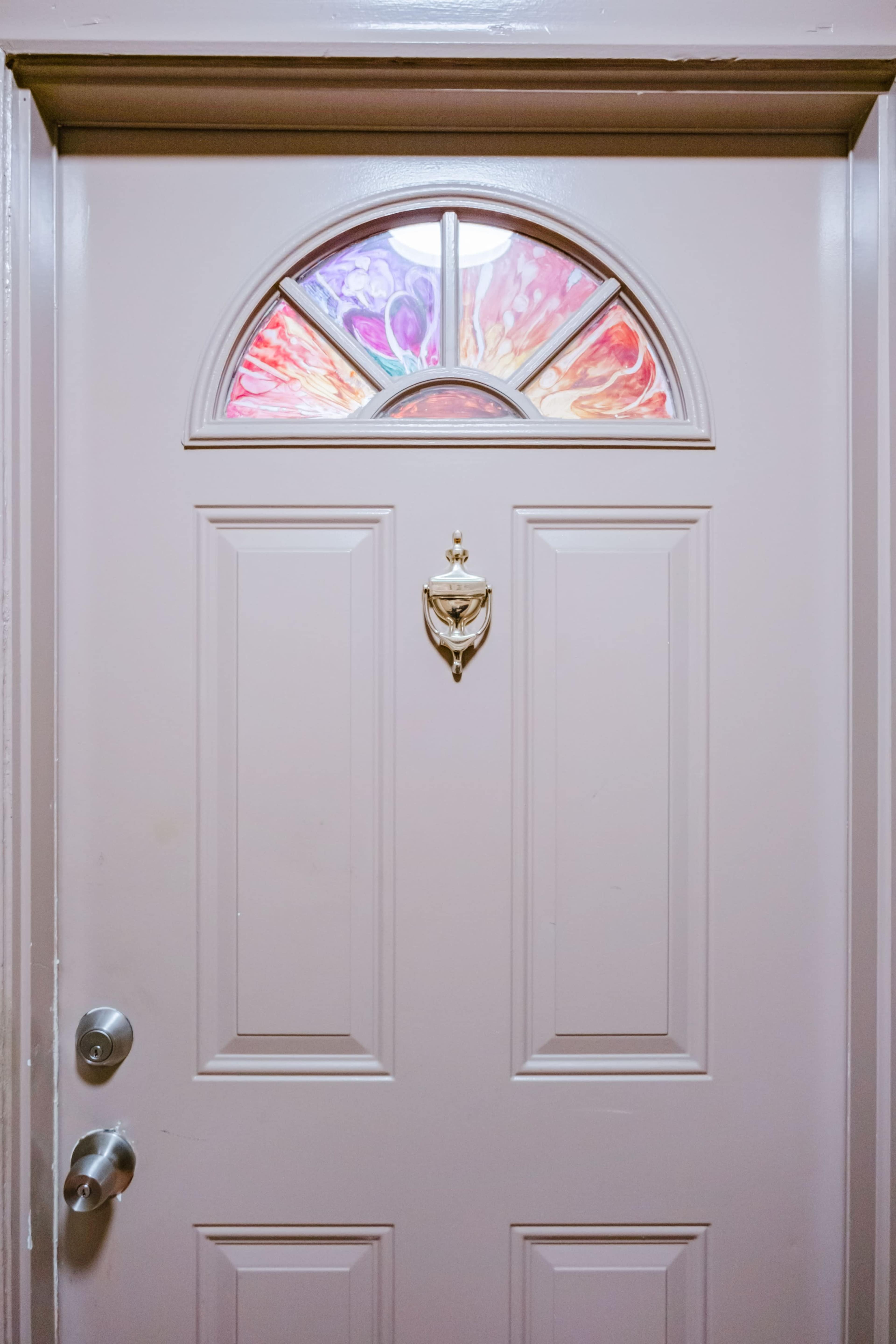 The image shows a closed, light-colored door with a decorative glass window at the top and a brass door knocker.