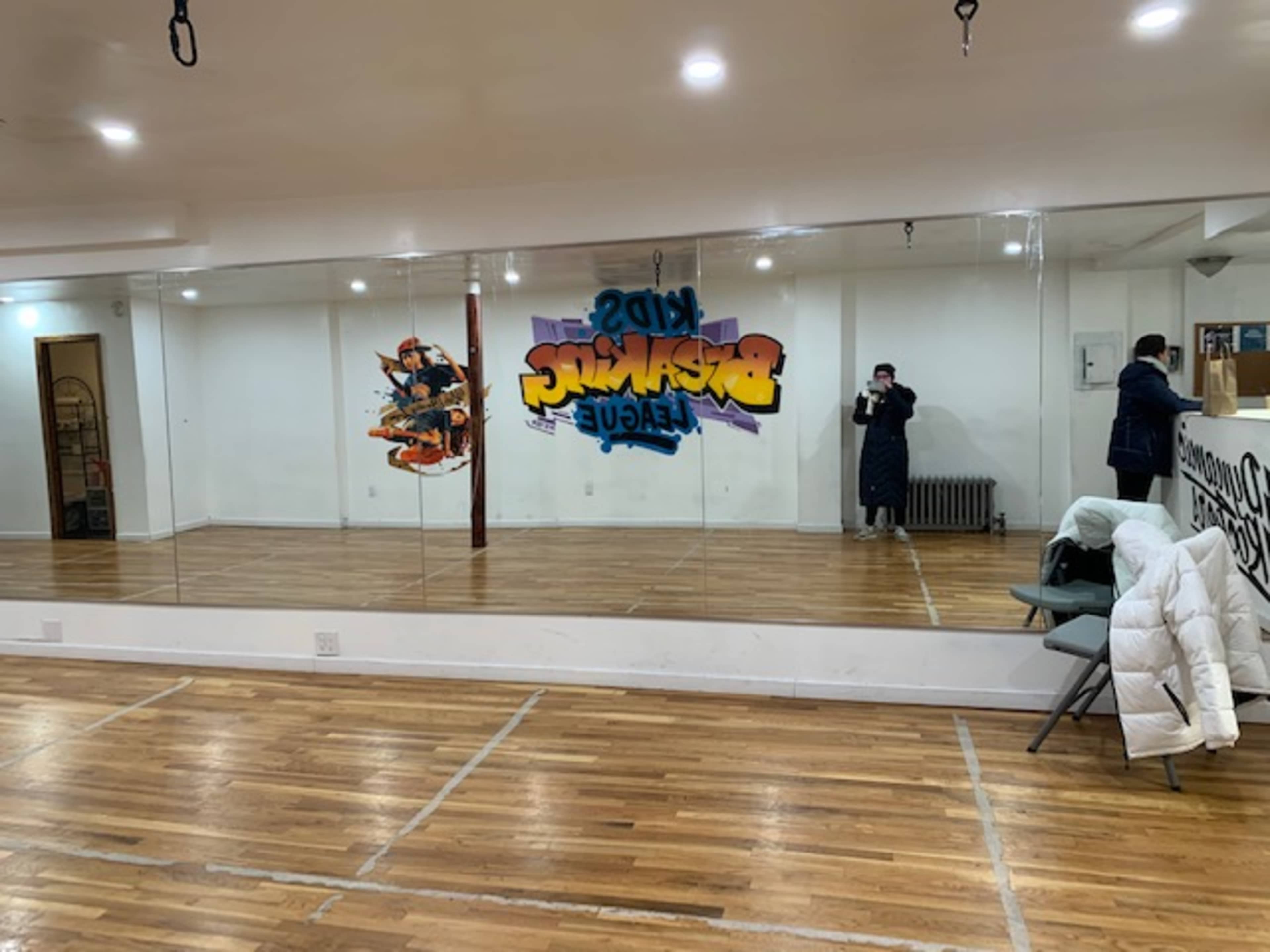 A dance studio with a large mirror, wooden flooring, and graffiti-style wall art.