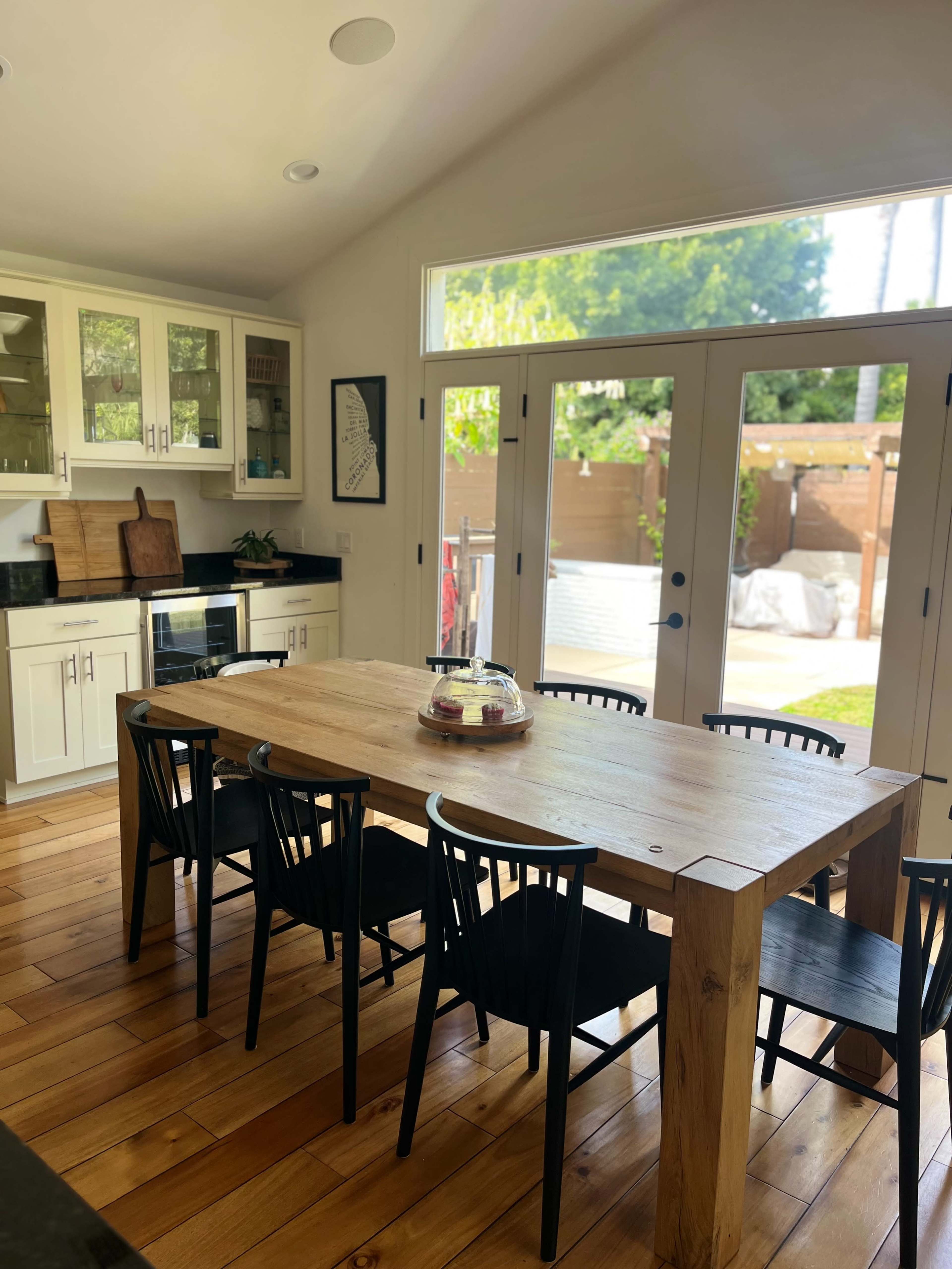 A spacious kitchen features a wooden dining table surrounded by black chairs, with large glass doors leading to an outdoor area.