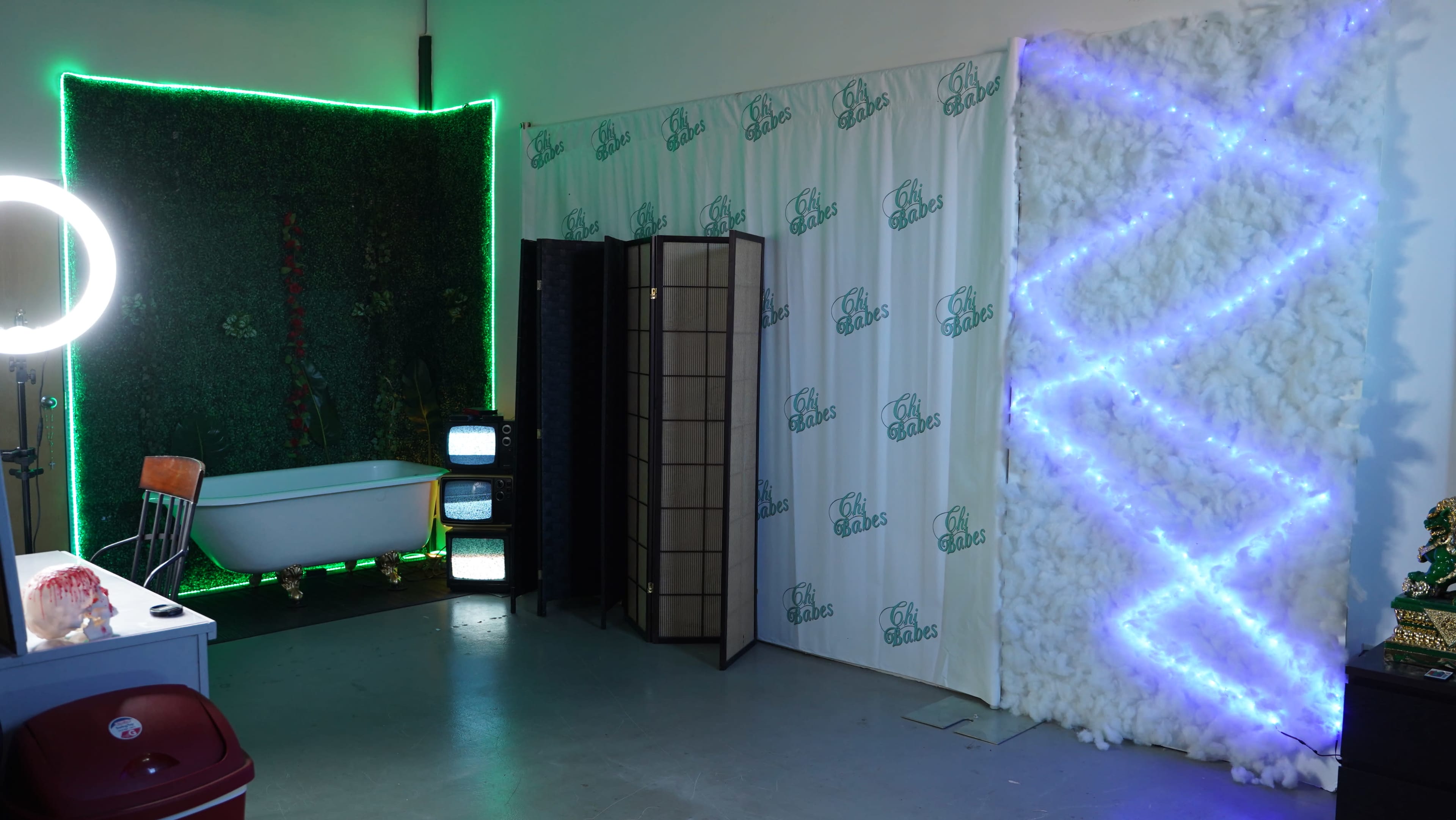 The scene features a room with a bathtub, a partition screen, two vintage television sets, and illuminated wall sections adorned with greenery and soft, glowing lights.