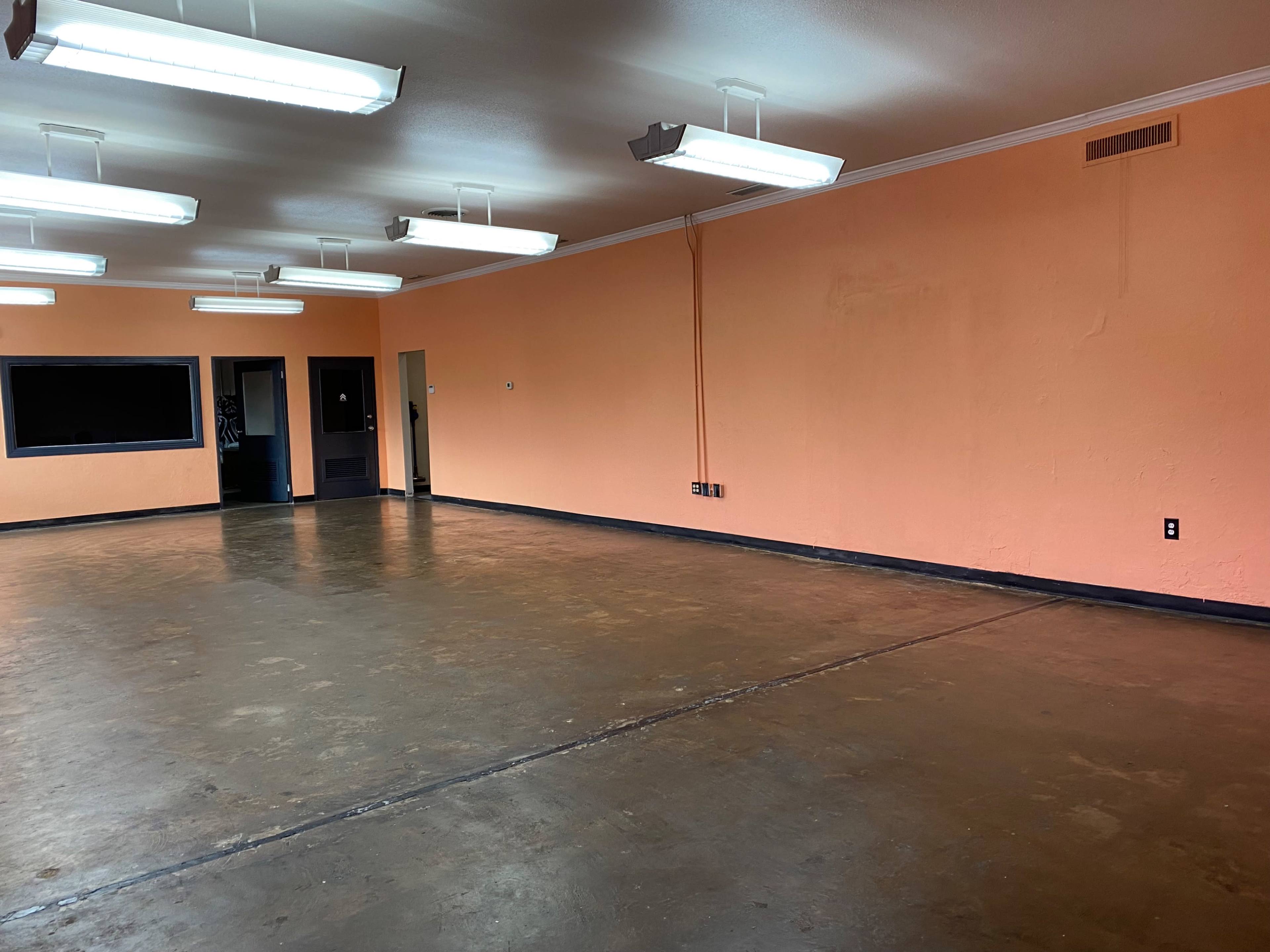 A spacious room with a polished concrete floor, orange walls, and fluorescent lighting.