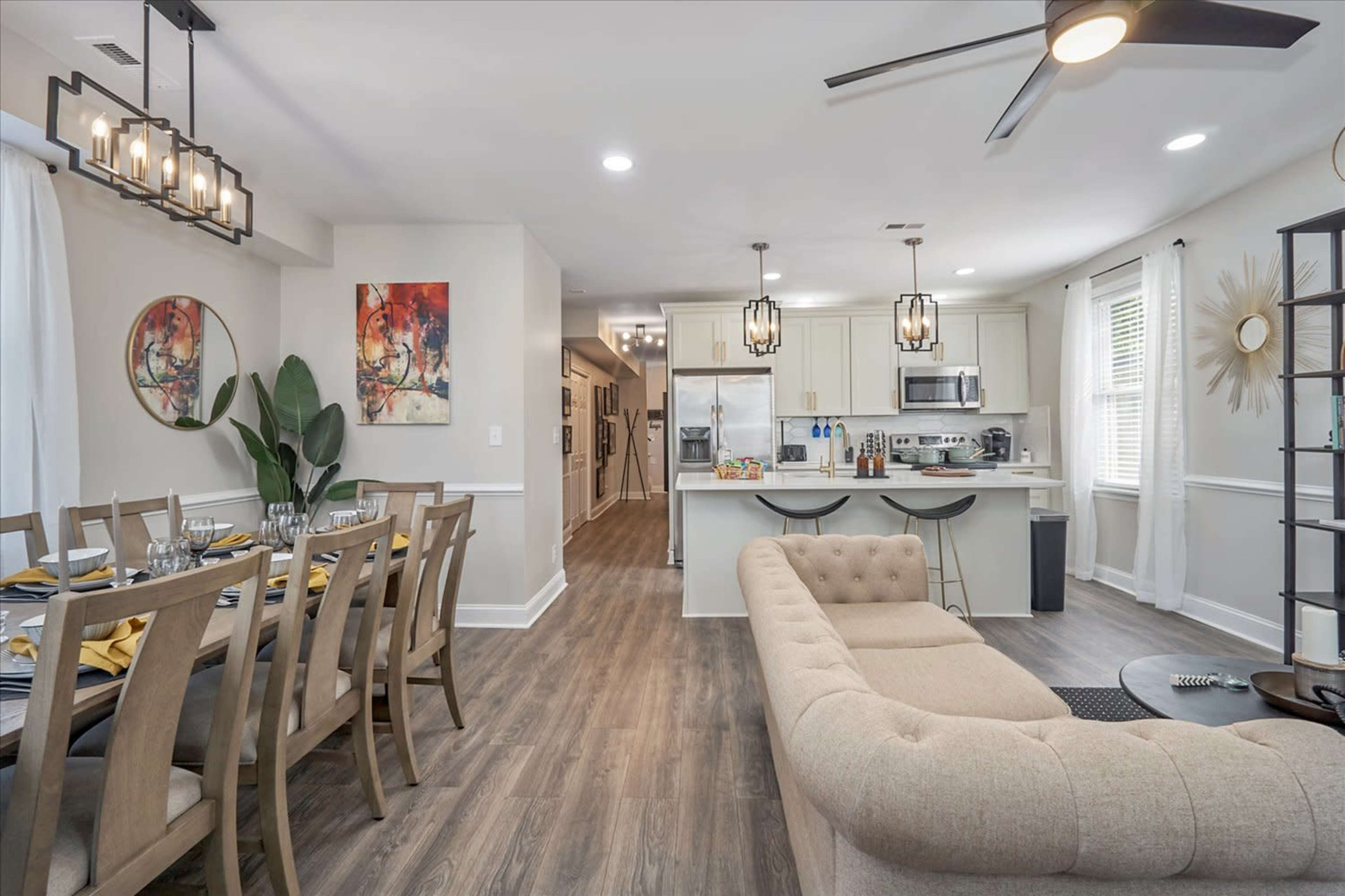 A modern open-concept living and dining area with a beige couch, a dining table set for meals, and a kitchen in the background.