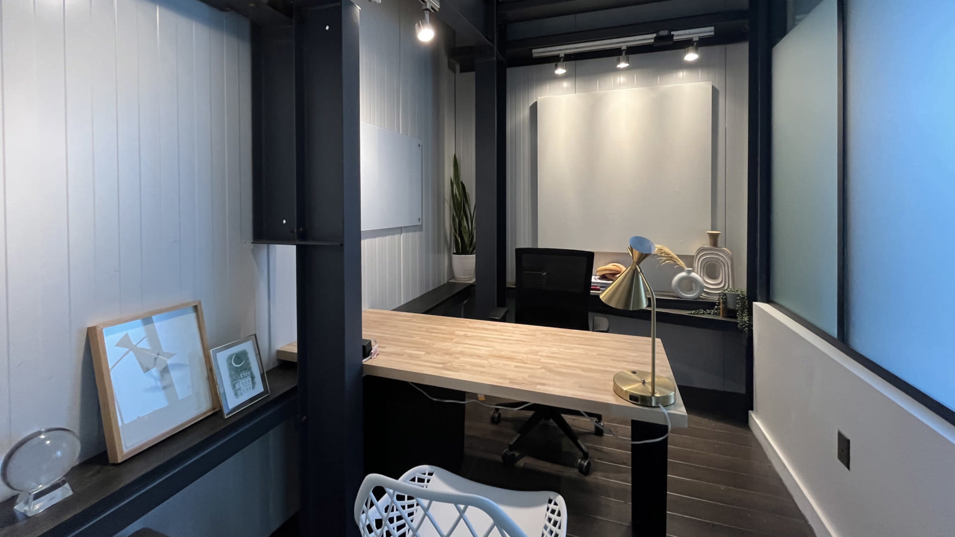 A modern office space with a wooden desk, a black office chair, and decorative elements, featuring minimalist design details and ample lighting.