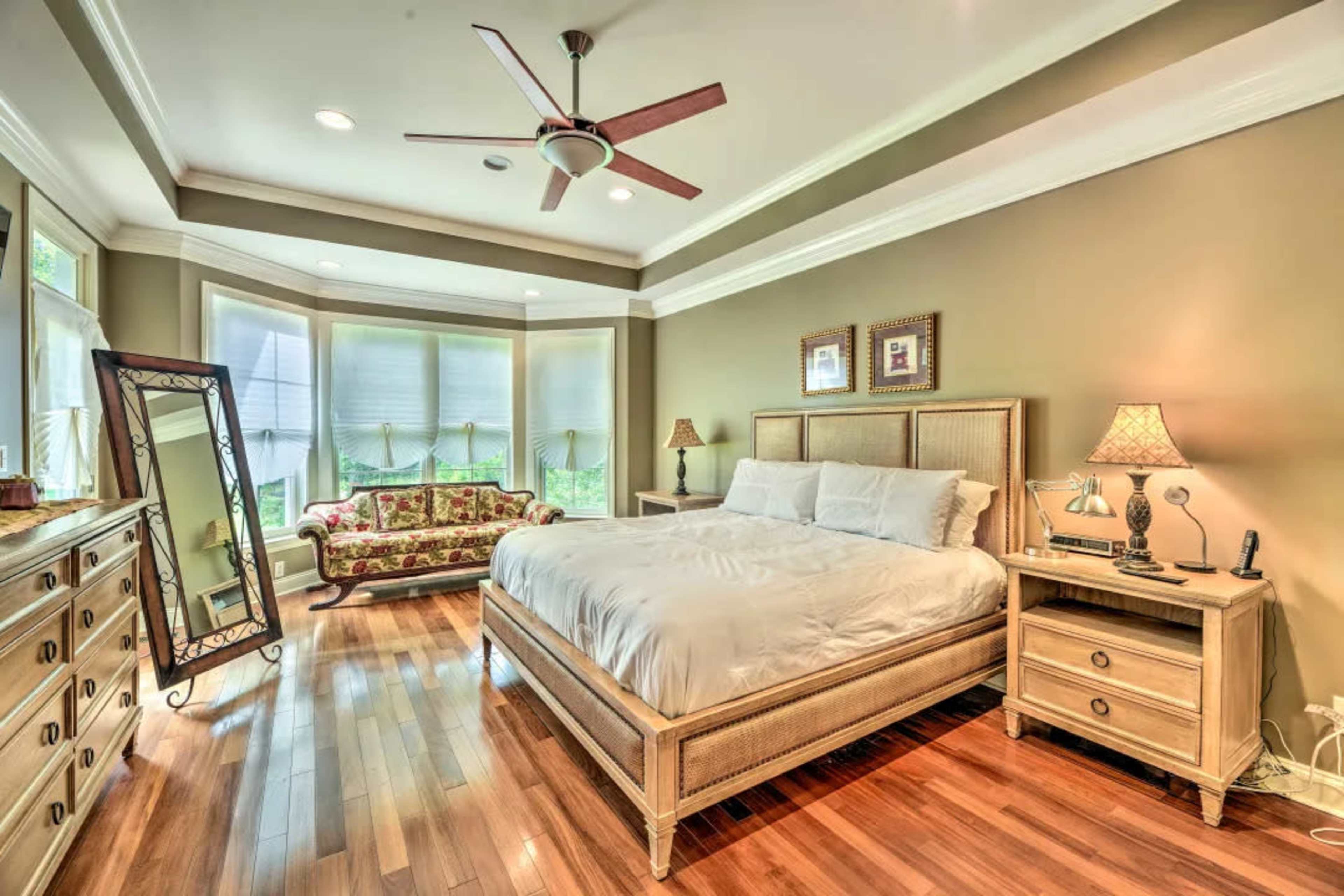 A well-furnished bedroom featuring a large bed, a dresser, a bedside table, and a decorative seating area with a mirror against the wall.