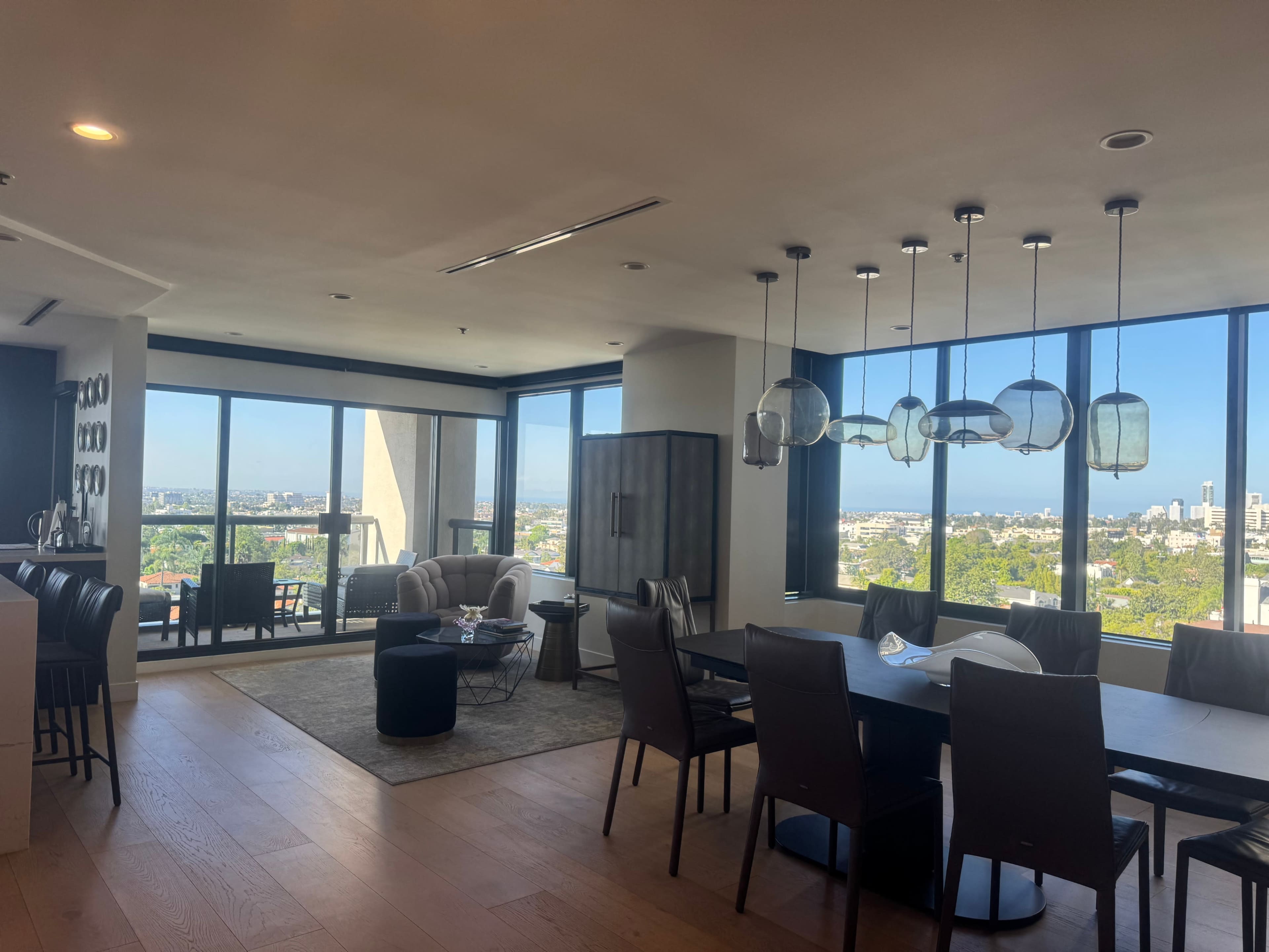 The image shows a modern interior of a stylish open-concept living and dining space with large windows offering a view of the city.