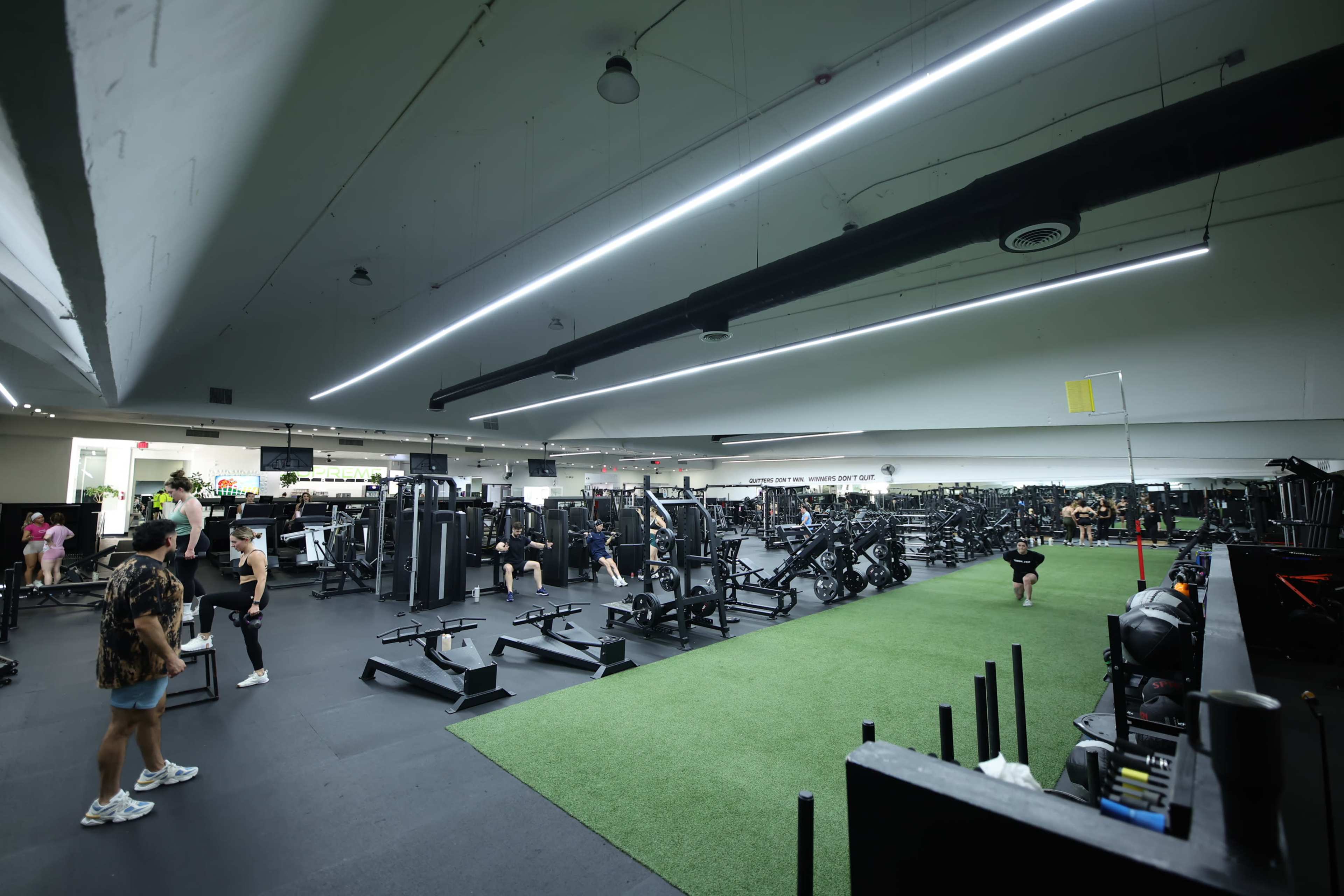 A fitness gym features various workout equipment and training areas, with individuals engaged in exercise.