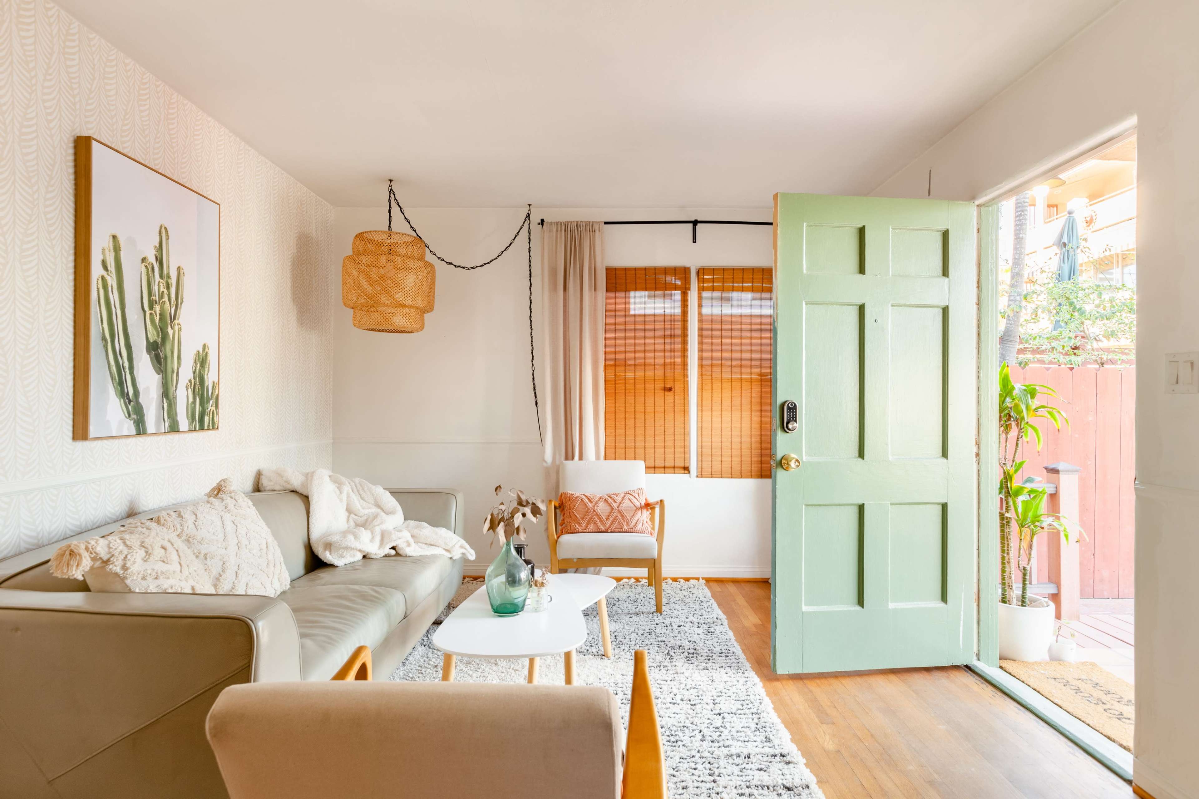 A bright, inviting living room with a light green door open to an outdoor space, featuring a sofa, a small table, and a decorative light fixture.
